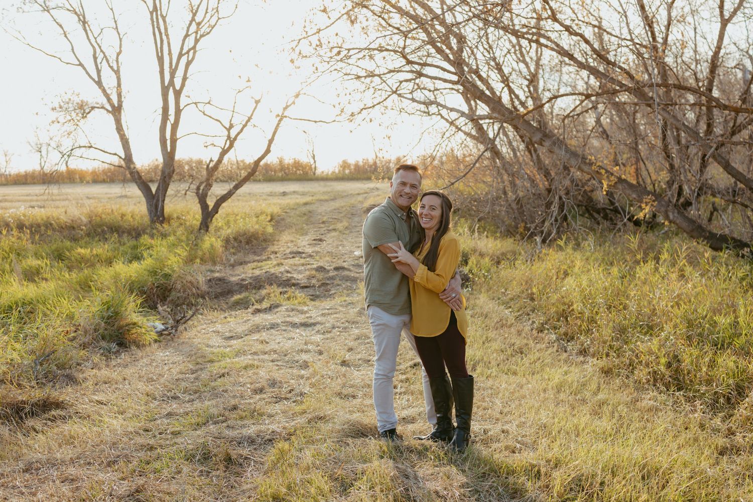 Two people walking together through a scenic field with bare trees in autumn.