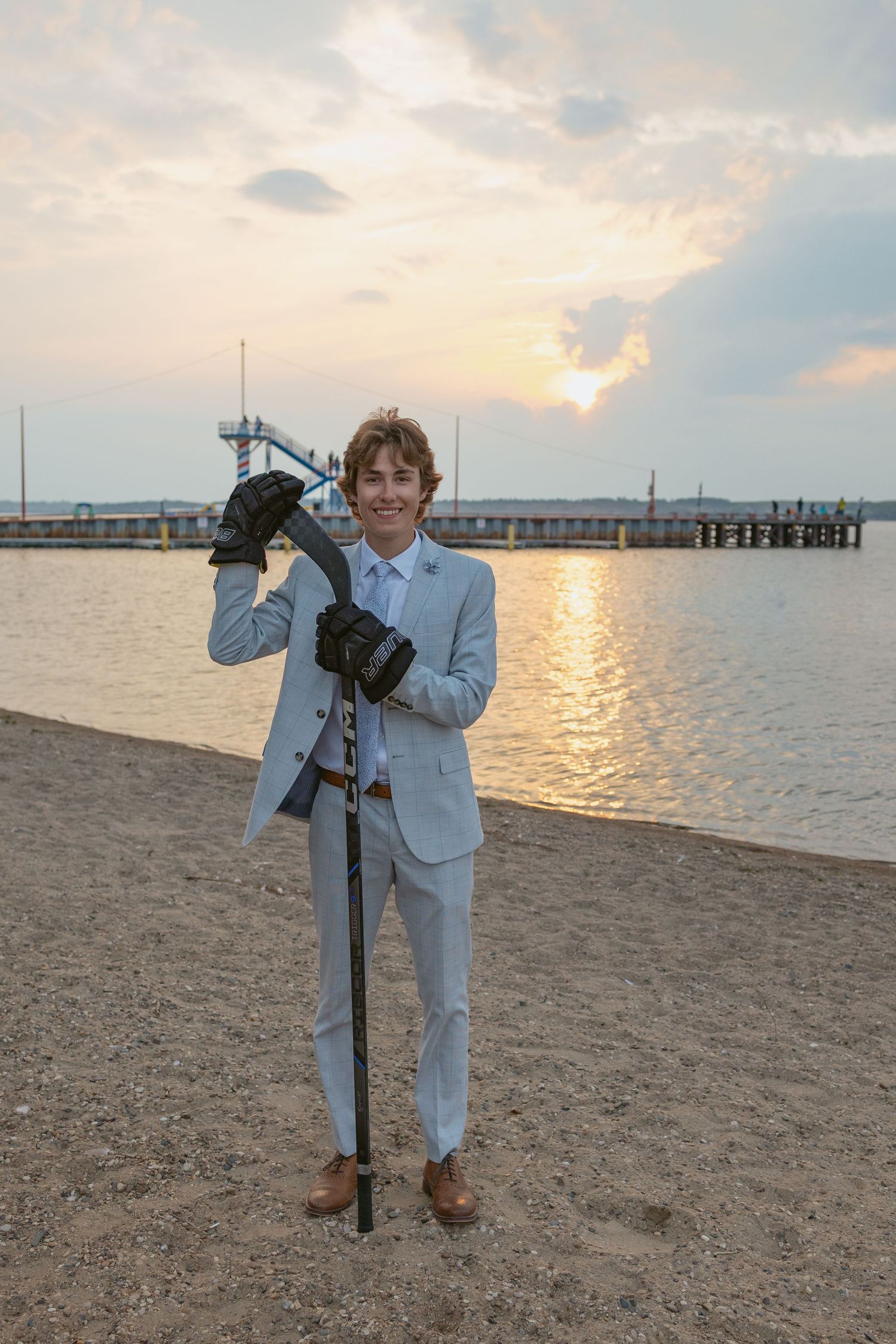 Figure in light blue suit poses with camera equipment on sandy beach at sunset.