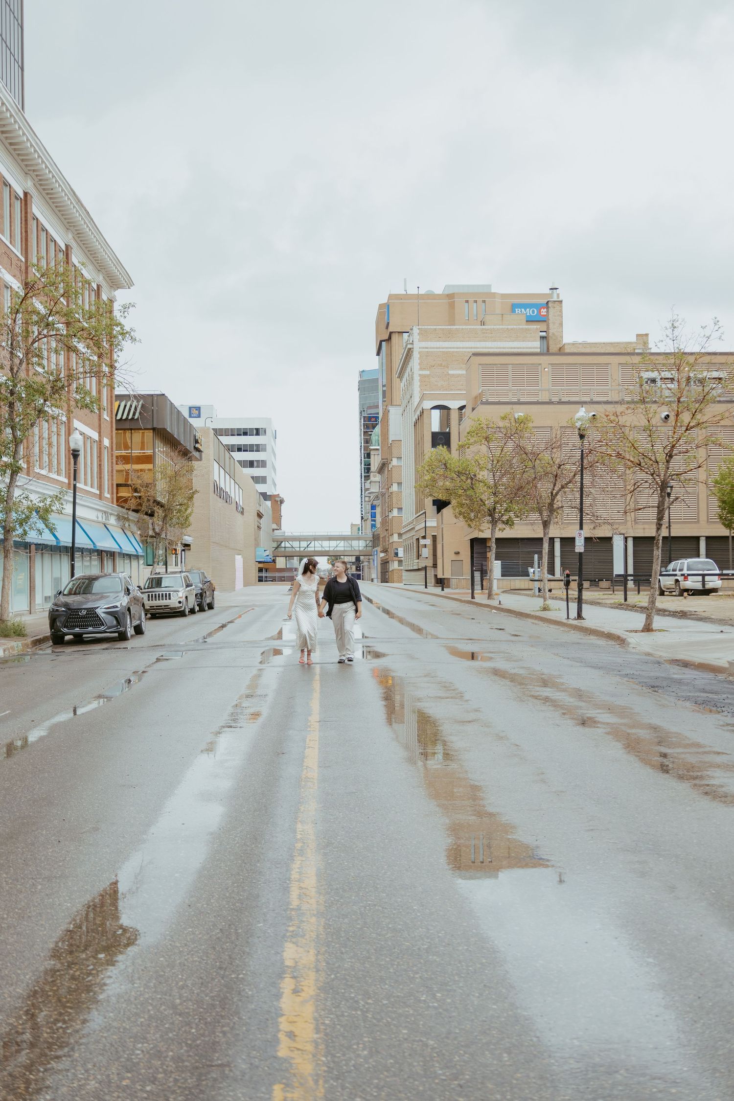 A wet city street after rain with buildings and storefronts lining both sides.
