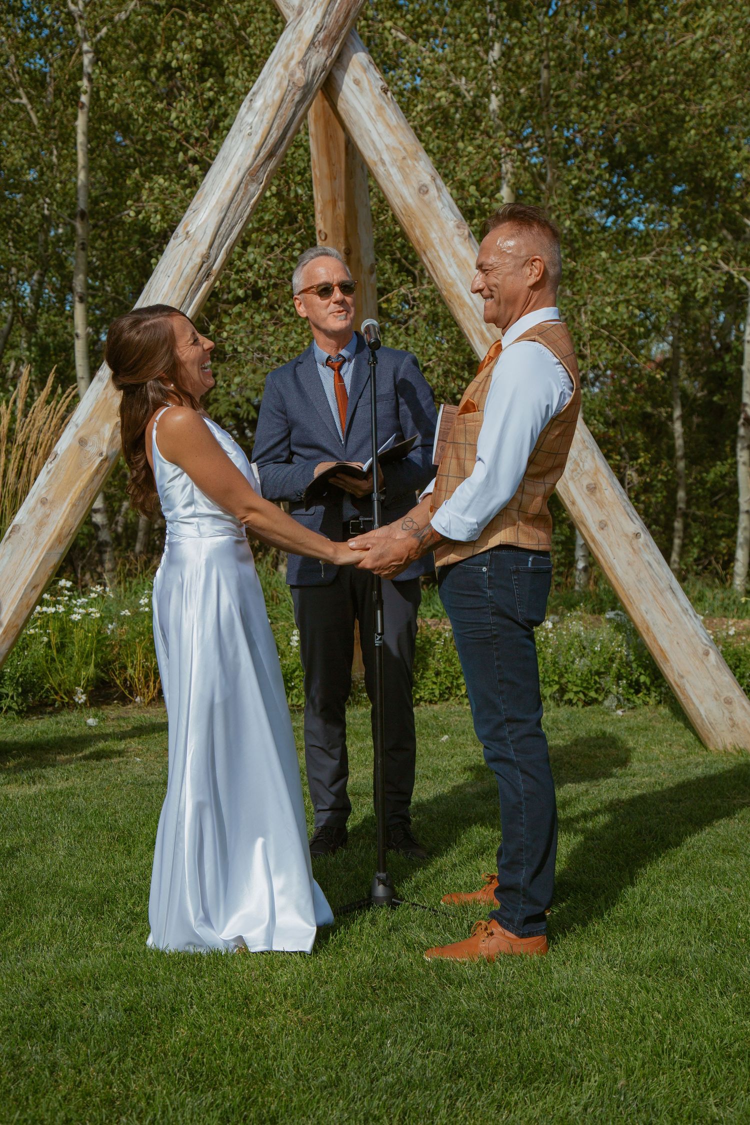 An intimate outdoor ceremony takes place under wooden beams surrounded by aspen trees.