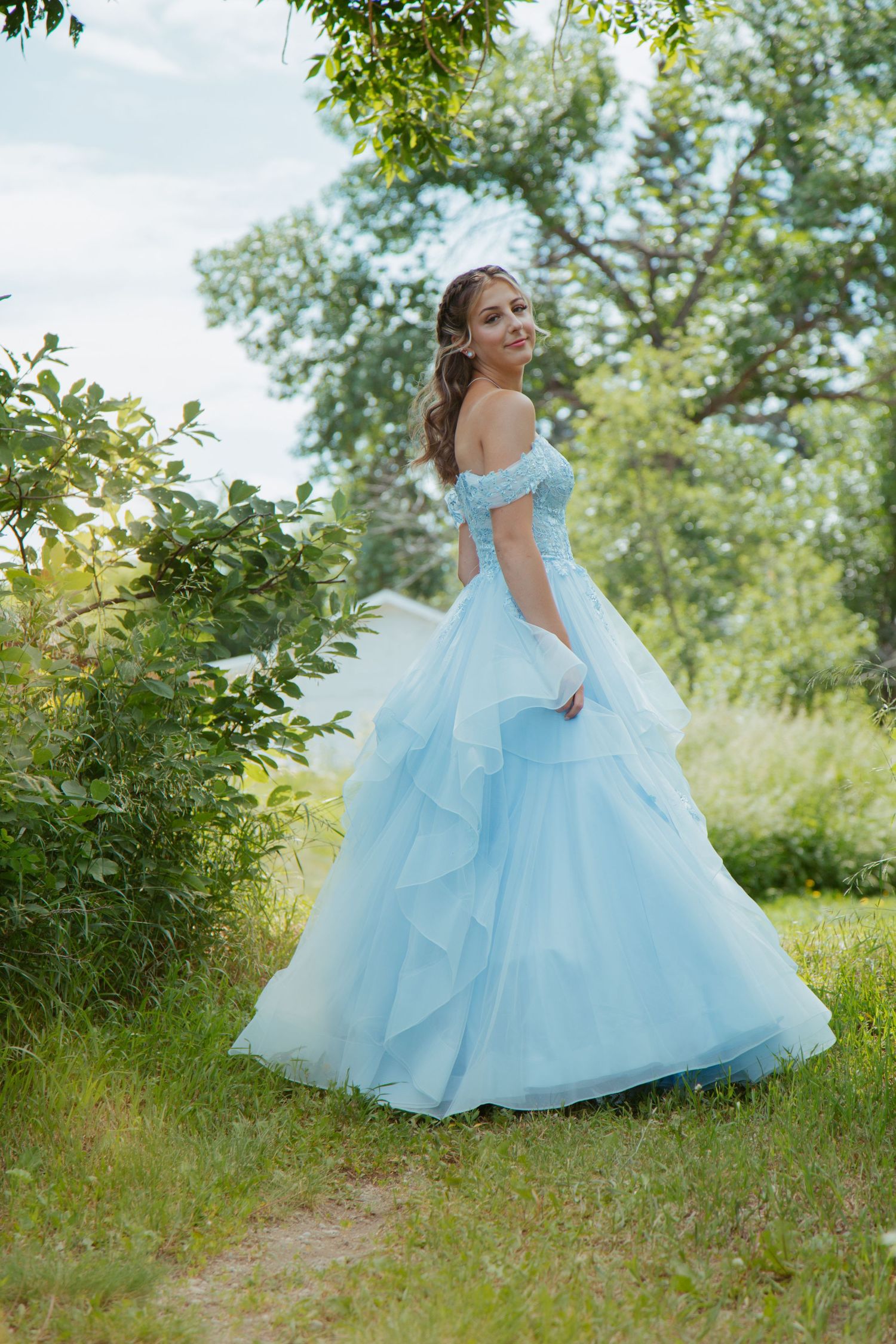 A flowing light blue princess ballgown photographed in motion against a natural outdoor setting.