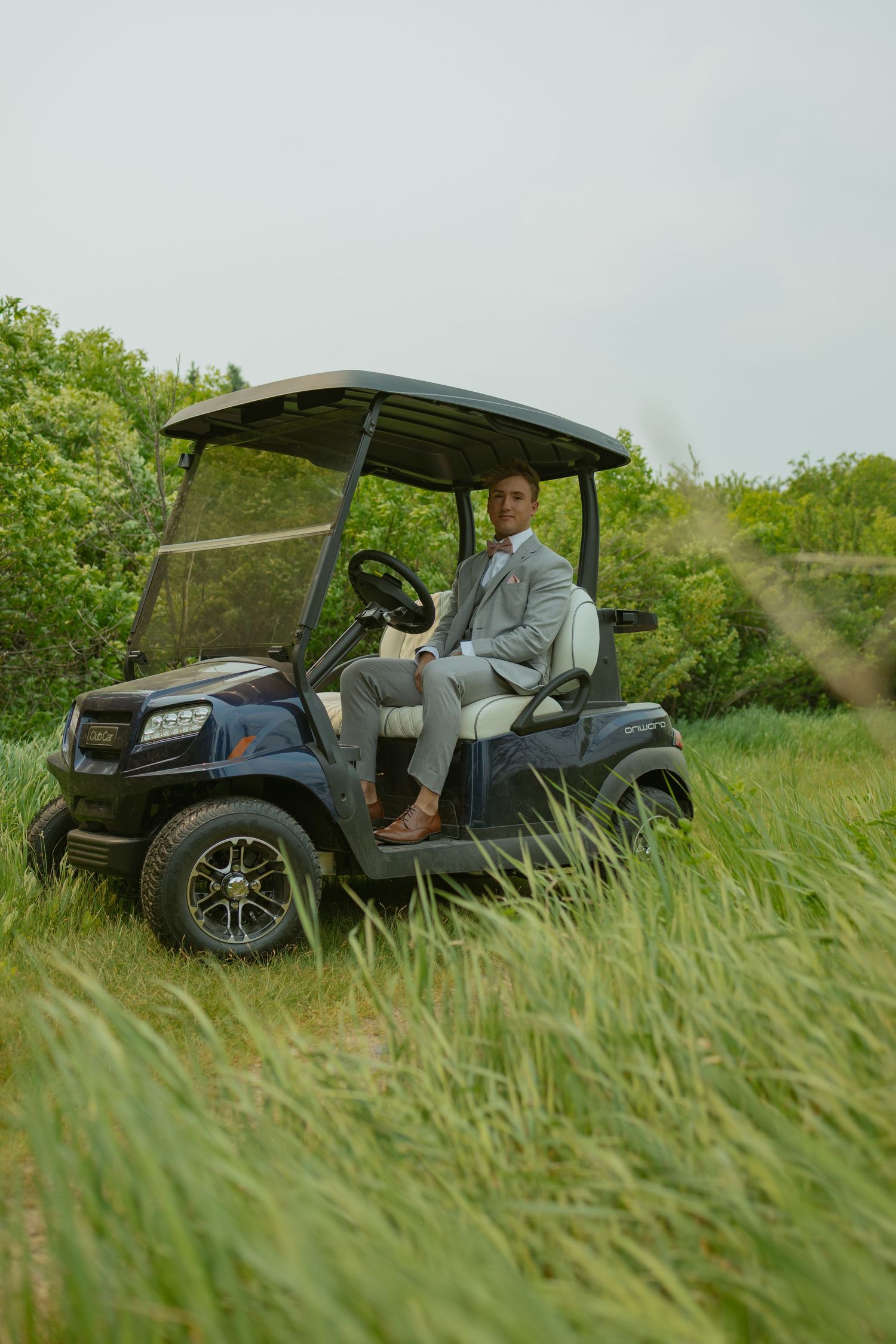 Golf cart driving through tall grass on a sunny day with lush green surroundings.