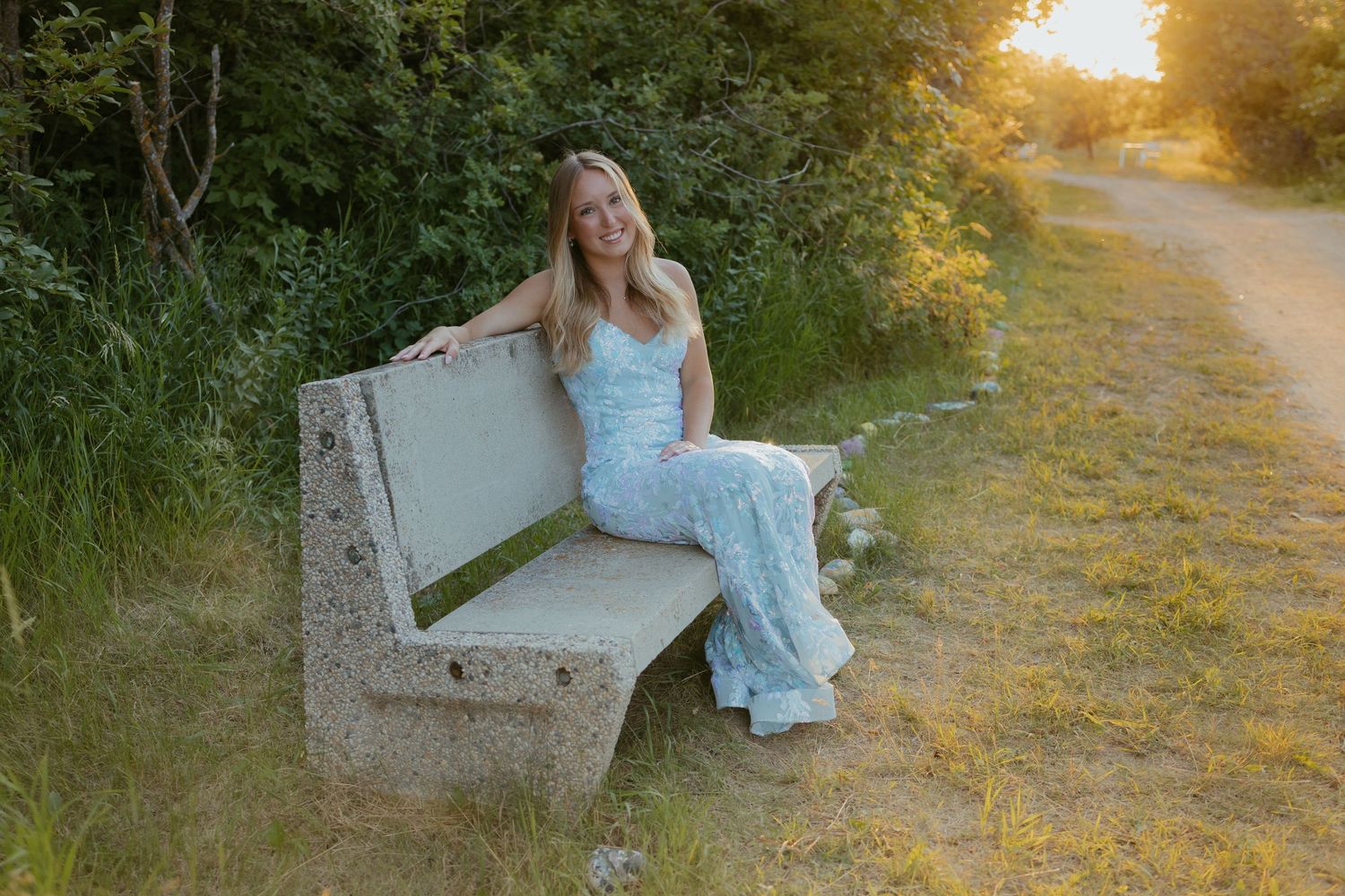 Person in blue dress sitting on stone bench at sunset in nature setting.