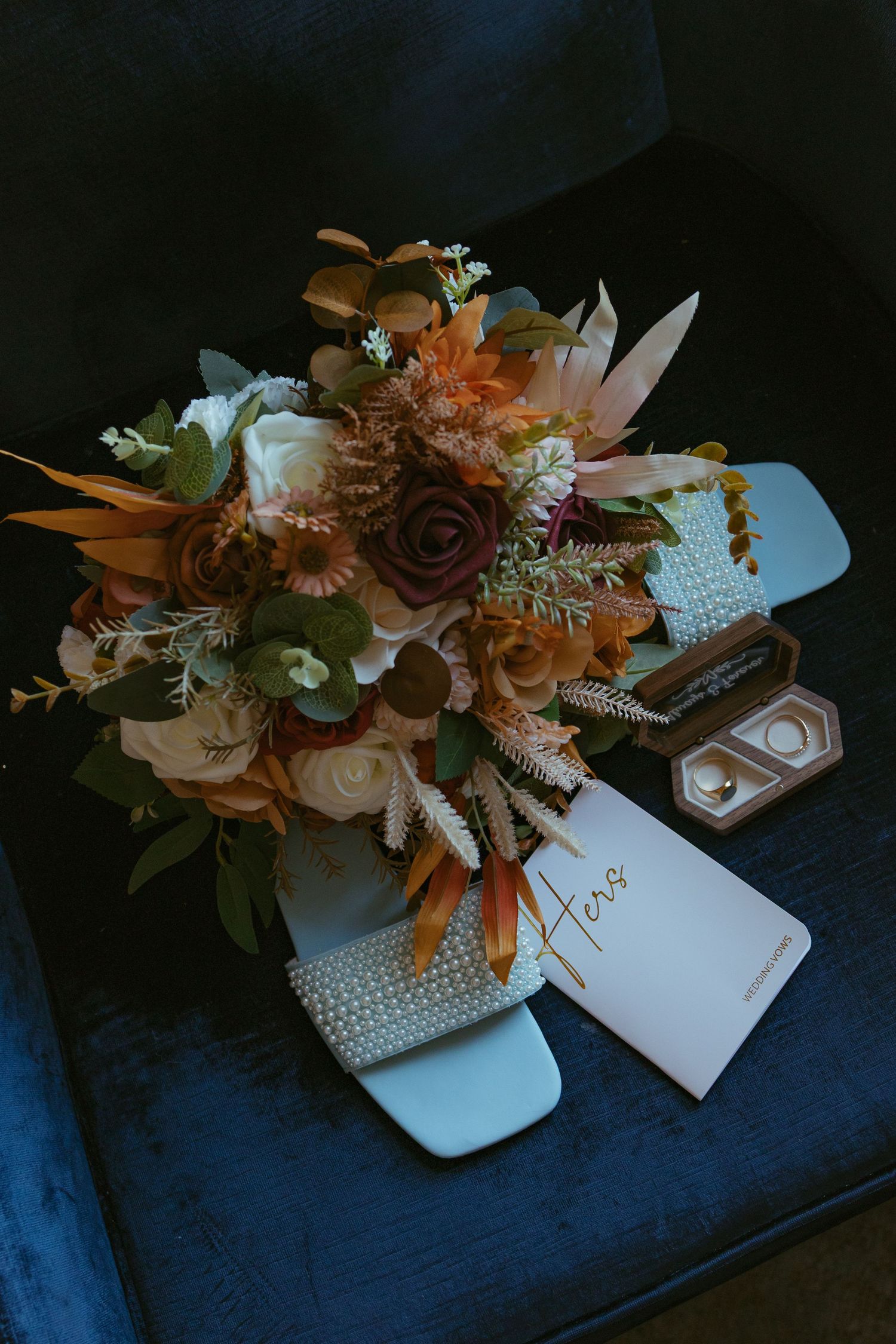 Floral arrangement with orange and white blooms next to wedding stationery on dark surface.