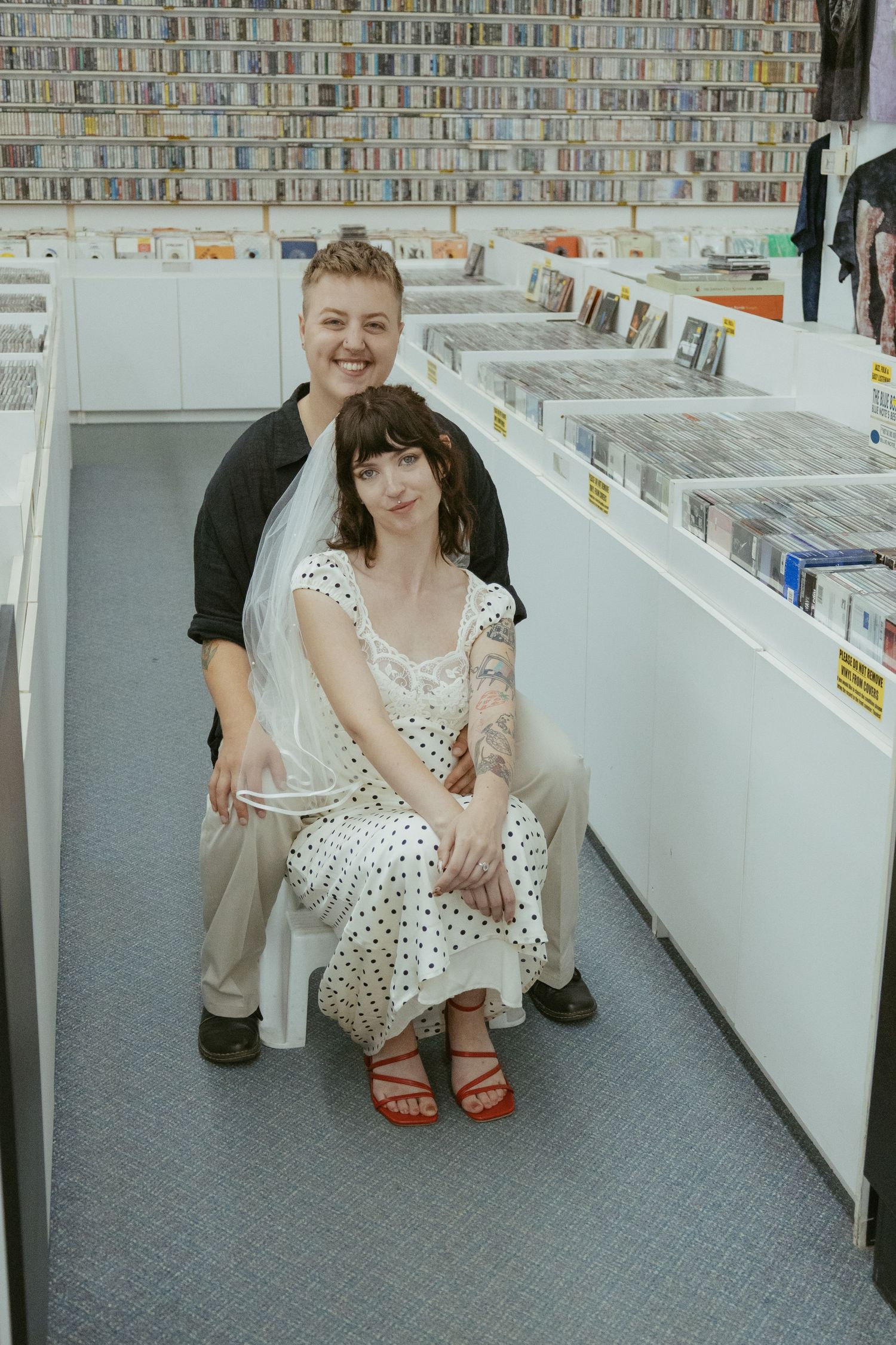 A person in a polka dot dress crouches between aisles of a record store.