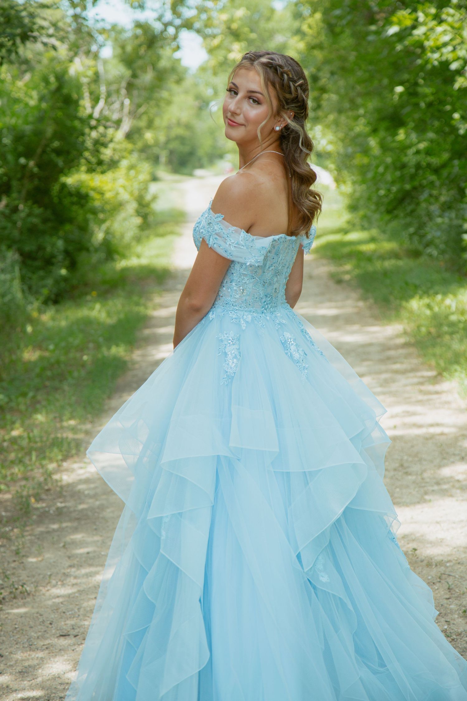 A light blue ballgown with ruffled layers and lace details photographed on a scenic nature path.