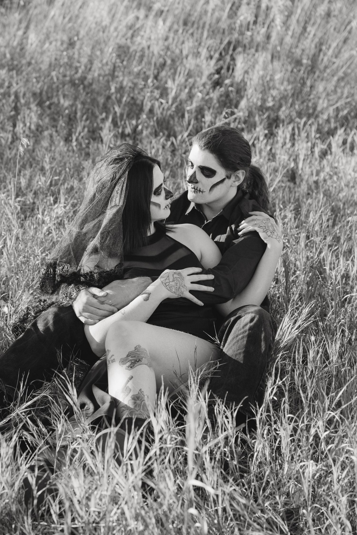 Gothic couple with face paint embracing in tall grass field in black and white.