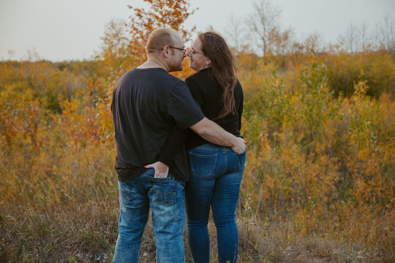 Intimate couple's portrait session in autumn field with golden trees.