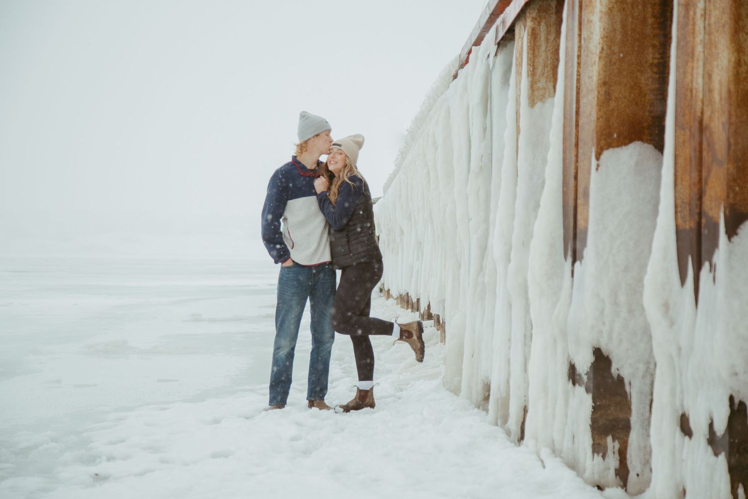 Couple standing by an ice-covered wall in winter clothing.