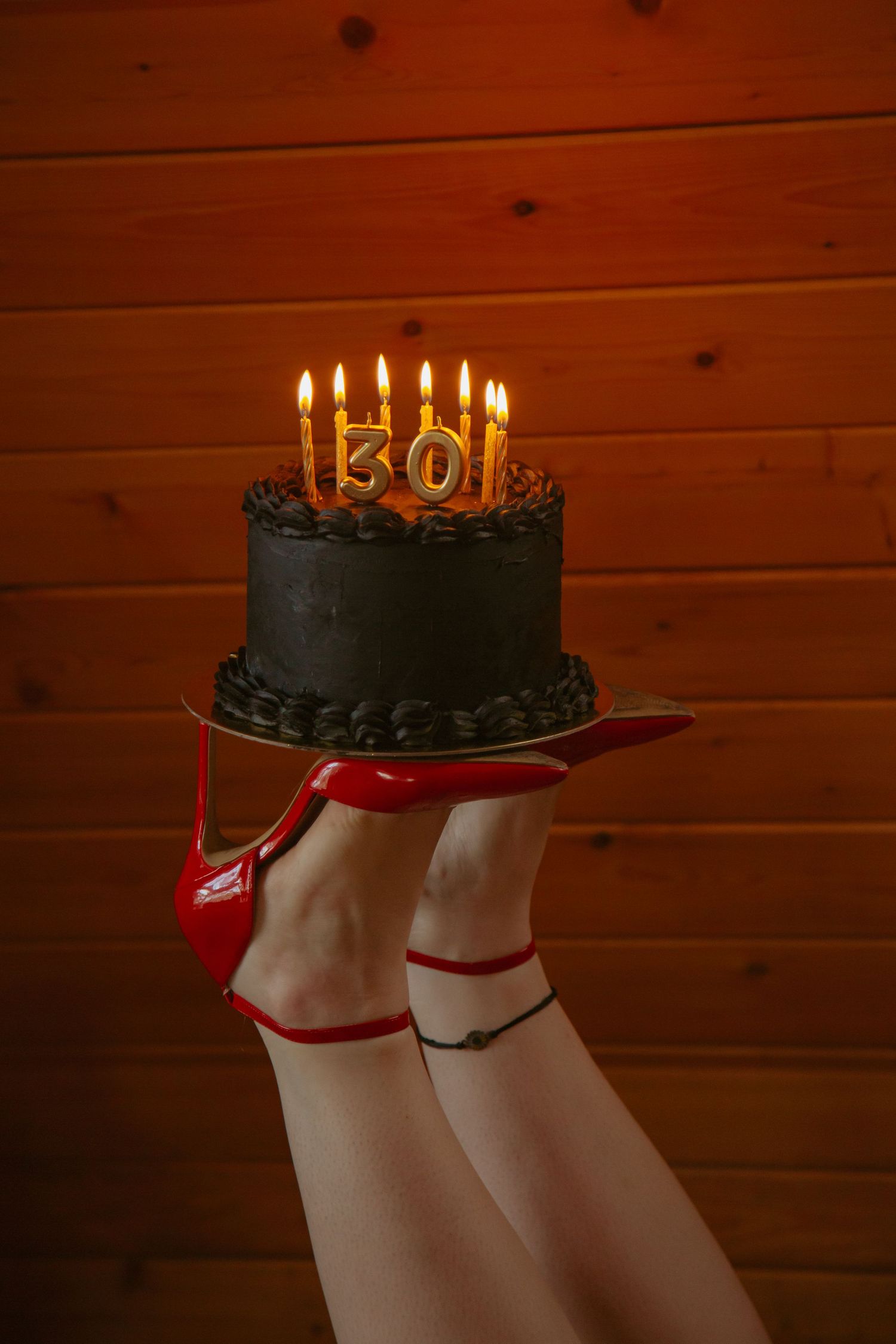 A chocolate birthday cake with lit candles against a wooden wall background.