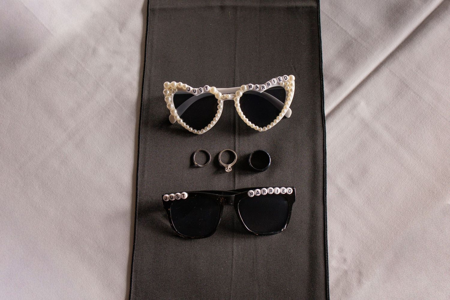 Wedding accessories featuring two pairs of decorative sunglasses and rings on dark background.