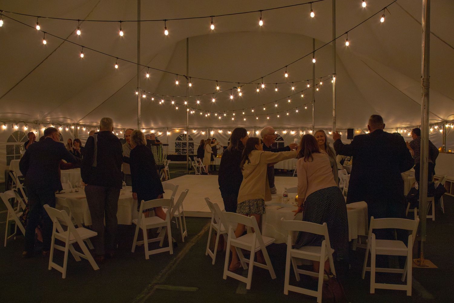 Wedding reception setup under a tent with rows of white chairs and twinkling lights.