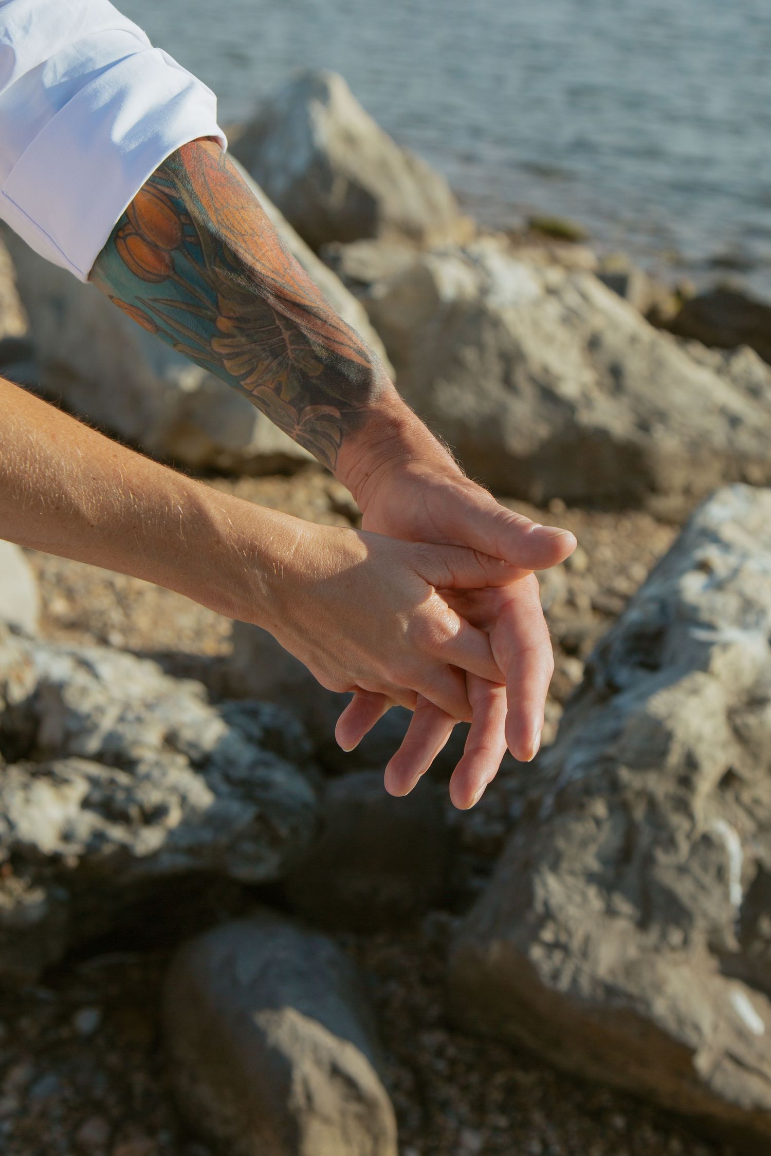 Close-up of hands resting on rocky coastal terrain with water in the background.