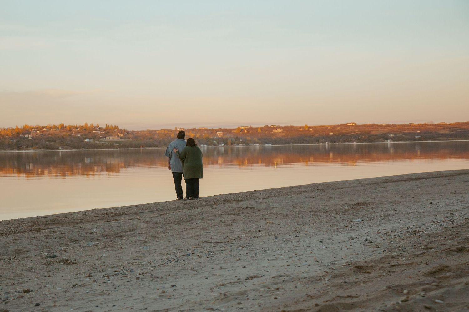 Silhouette of two people walking on beach during sunset with calm water in background.