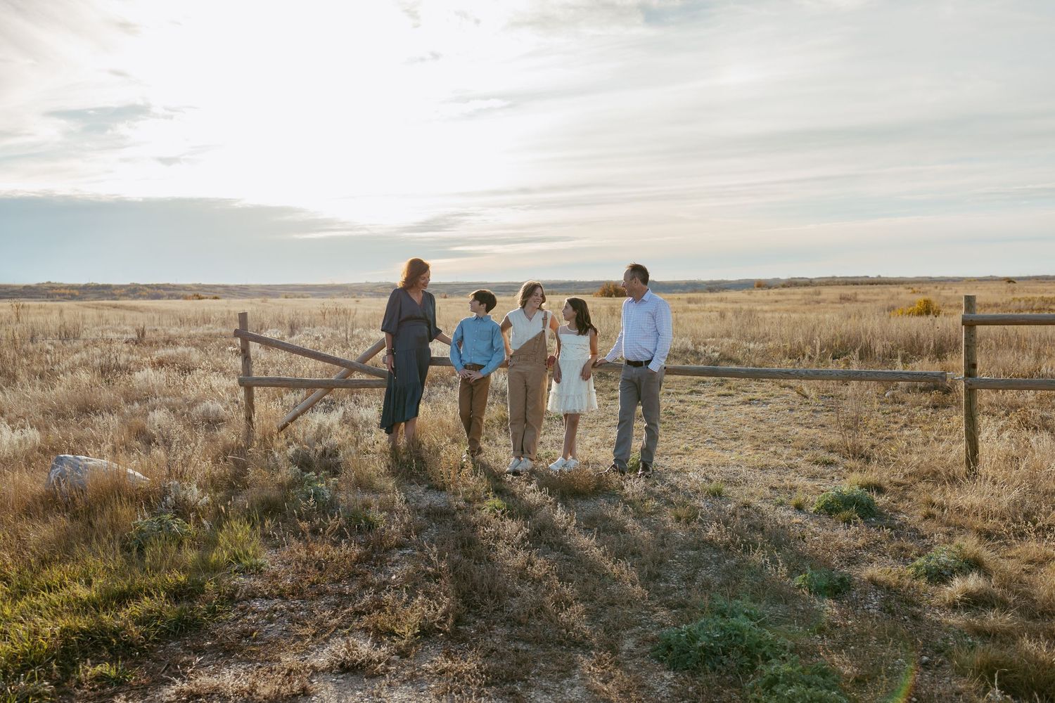 A family stands together on a grassy hill during golden hour with long shadows cast behind them.