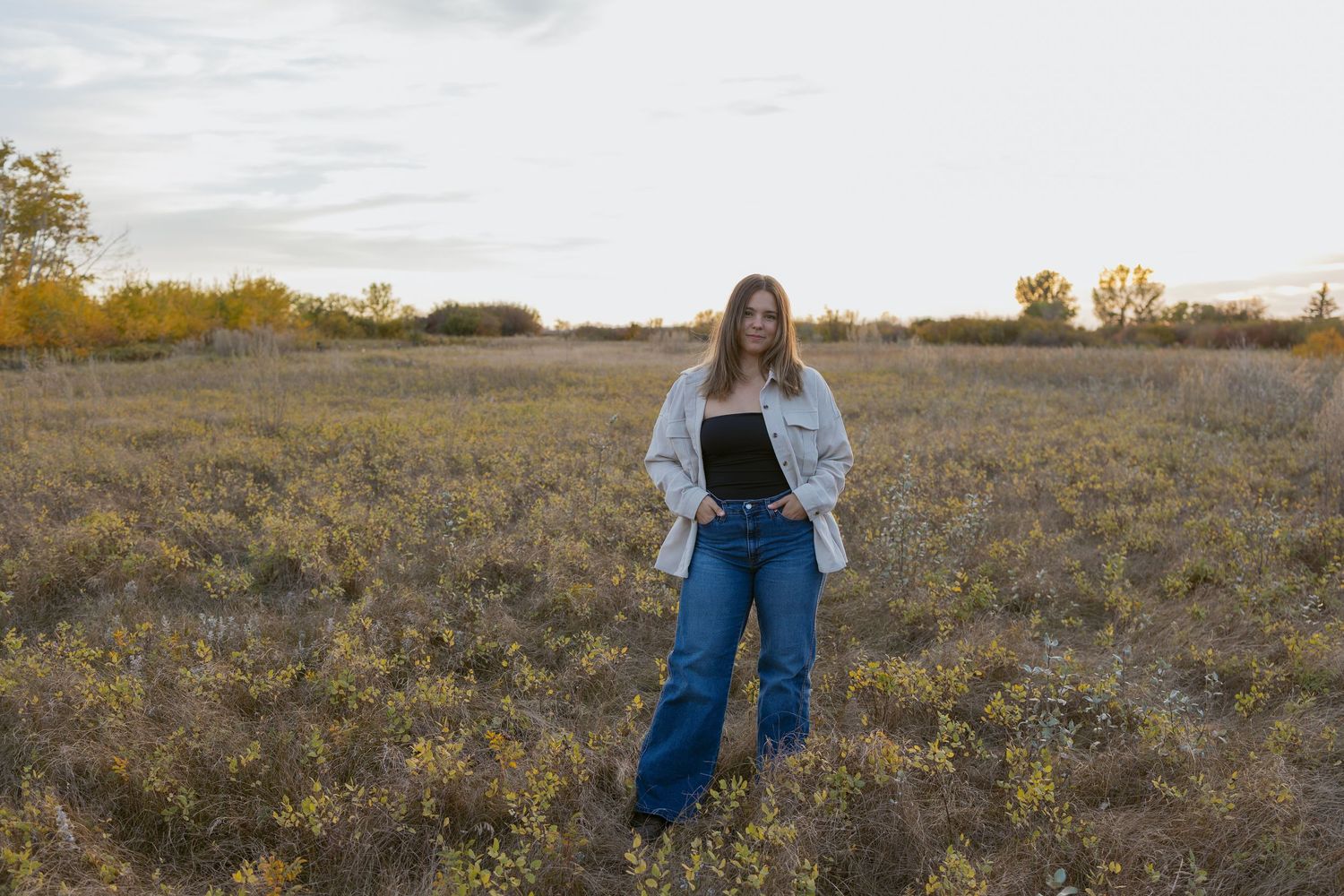 Person in denim and white shirt exploring a scenic autumn meadow during sunset.