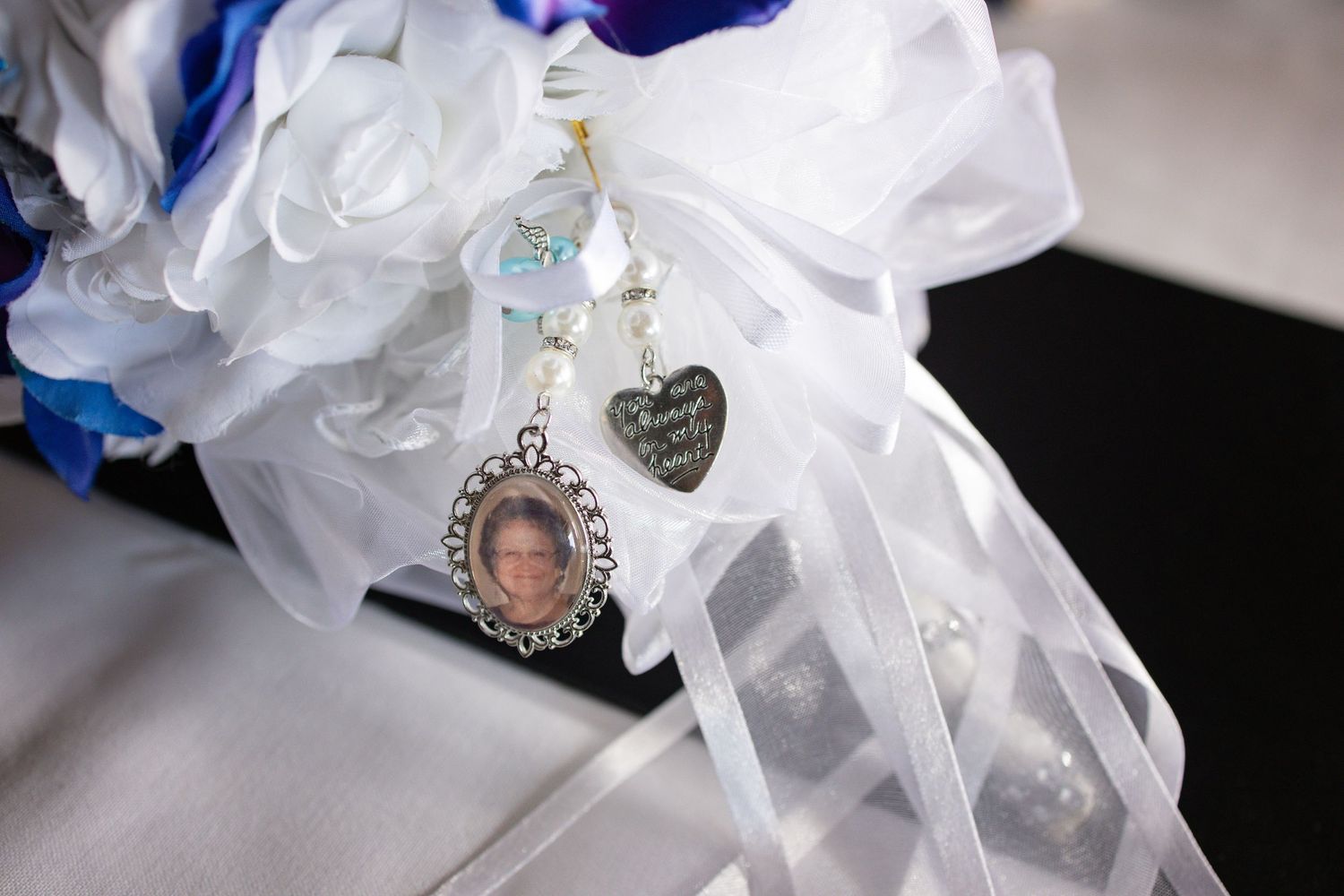 Wedding bouquet with white roses, blue flowers, and a memorial photo charm pendant with heart accents and ribbon.