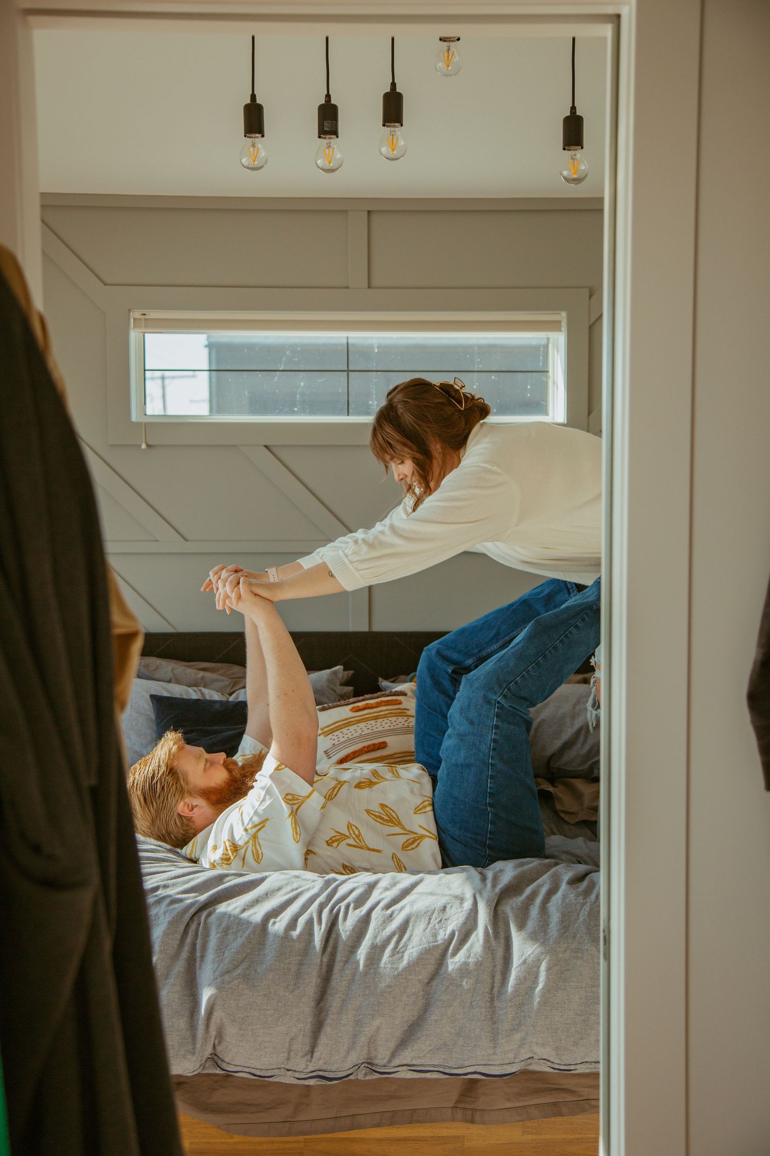 Playful couple moment captured through doorway with pendant lights above.