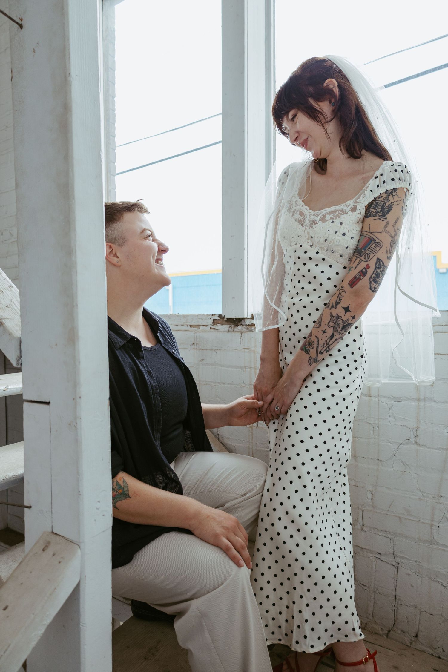 A couple shares tender moments in a sunlit white room with polka dot dress details.