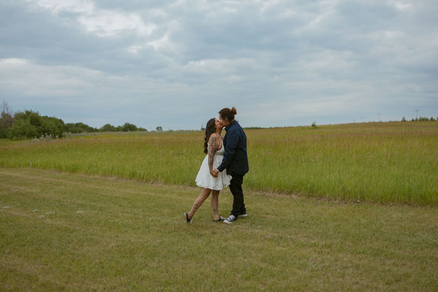 A couple embraces while standing on a grassy path with trees in the distance.