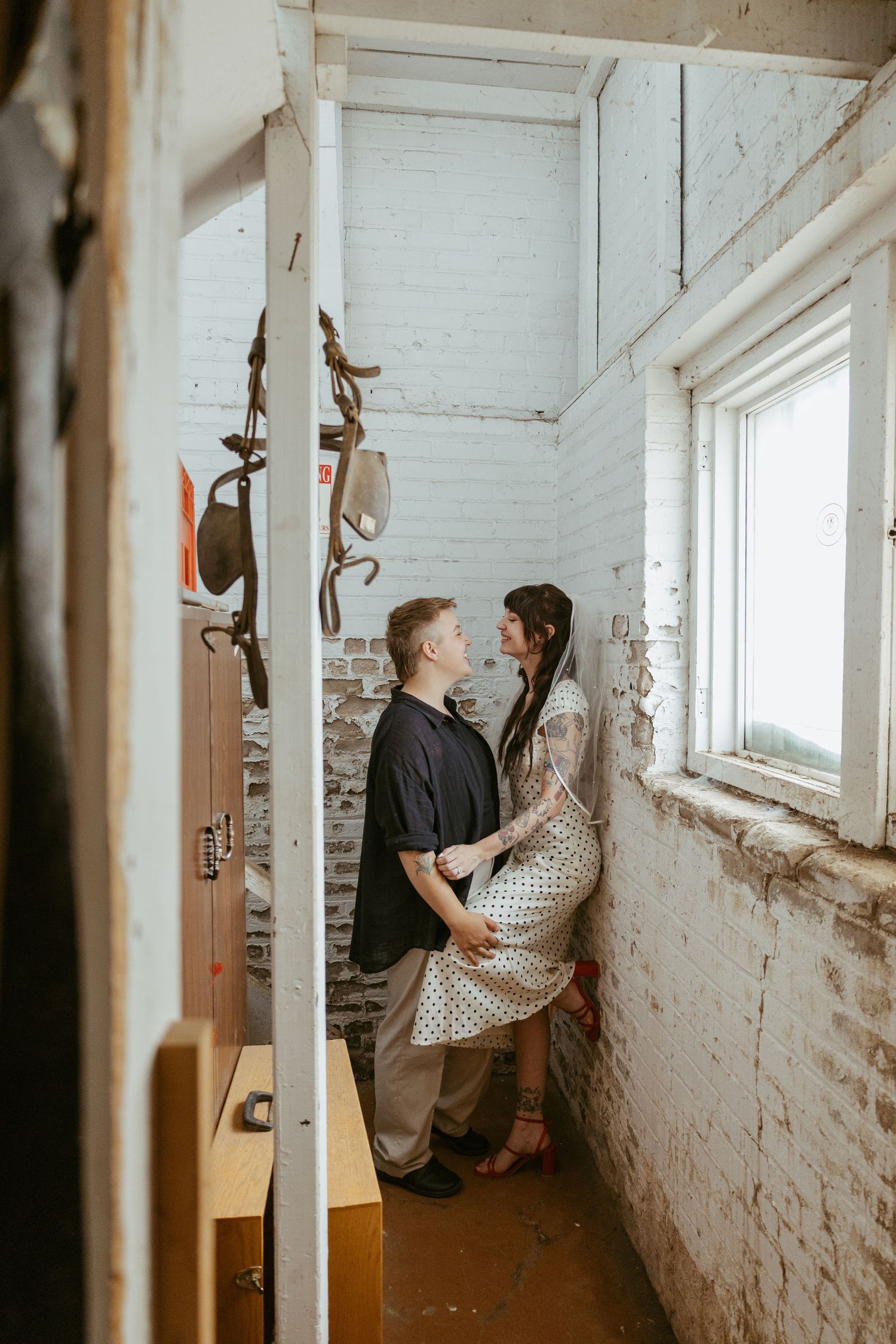 Couple sharing intimate moment by window in rustic white brick hallway.