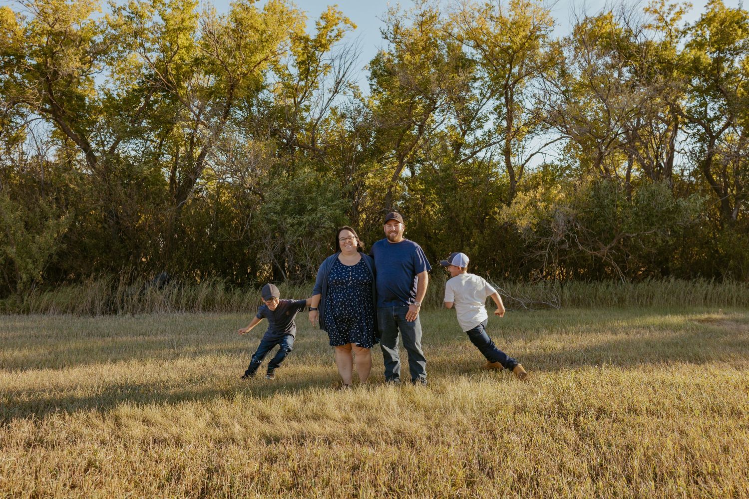 Family playing and running through golden autumn field during sunset.