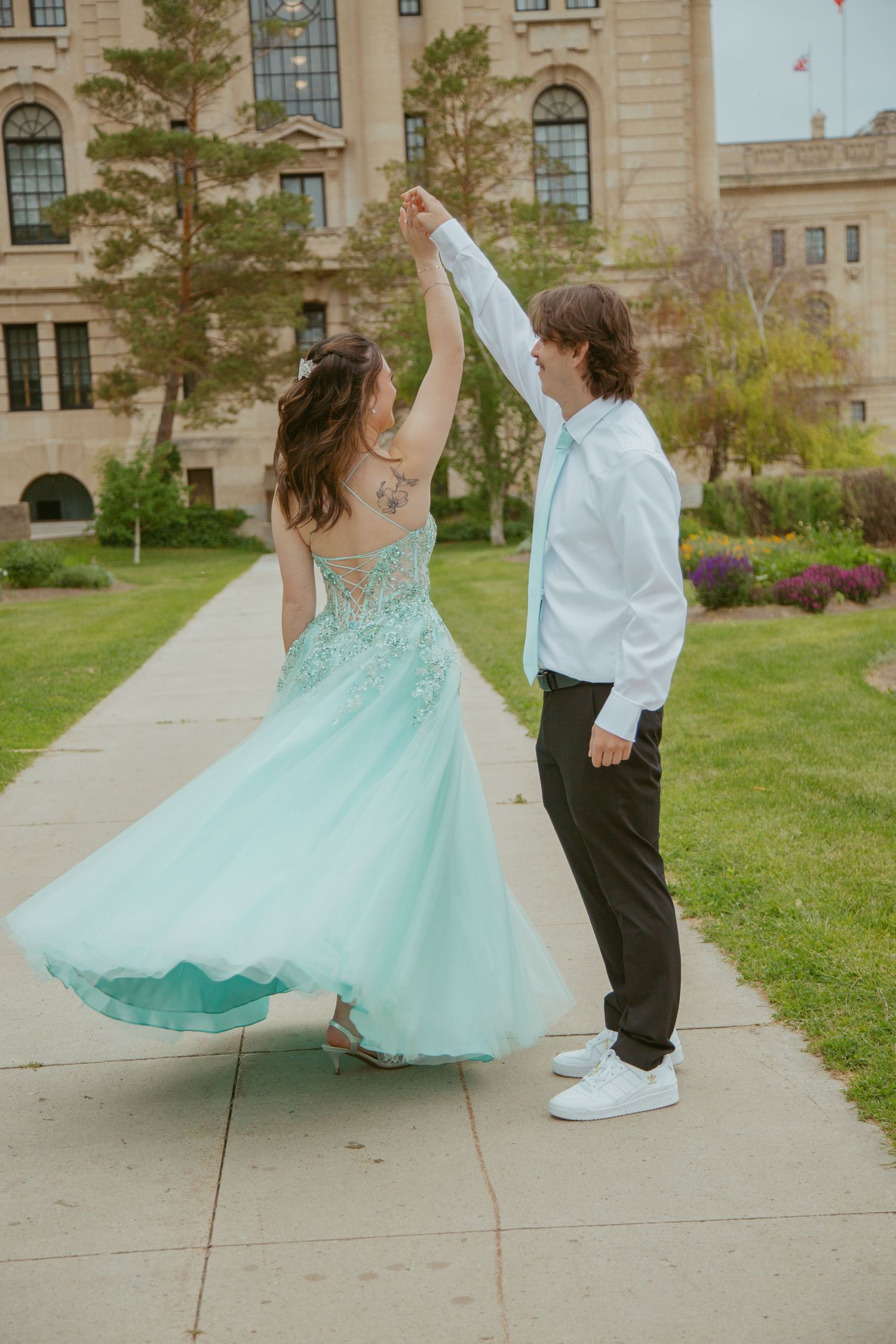Dancing sequence in mint formal wear on a pathway near historic building.