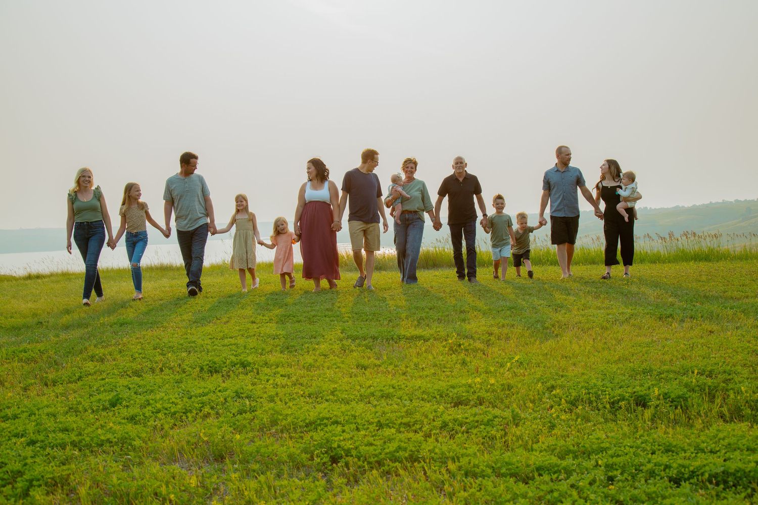 Silhouettes of people walking together across green hilltop against bright sky.