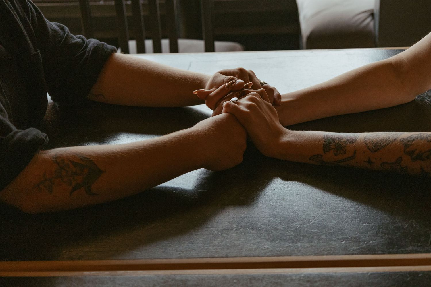 Close-up shot of hands reaching across a dark table surface.