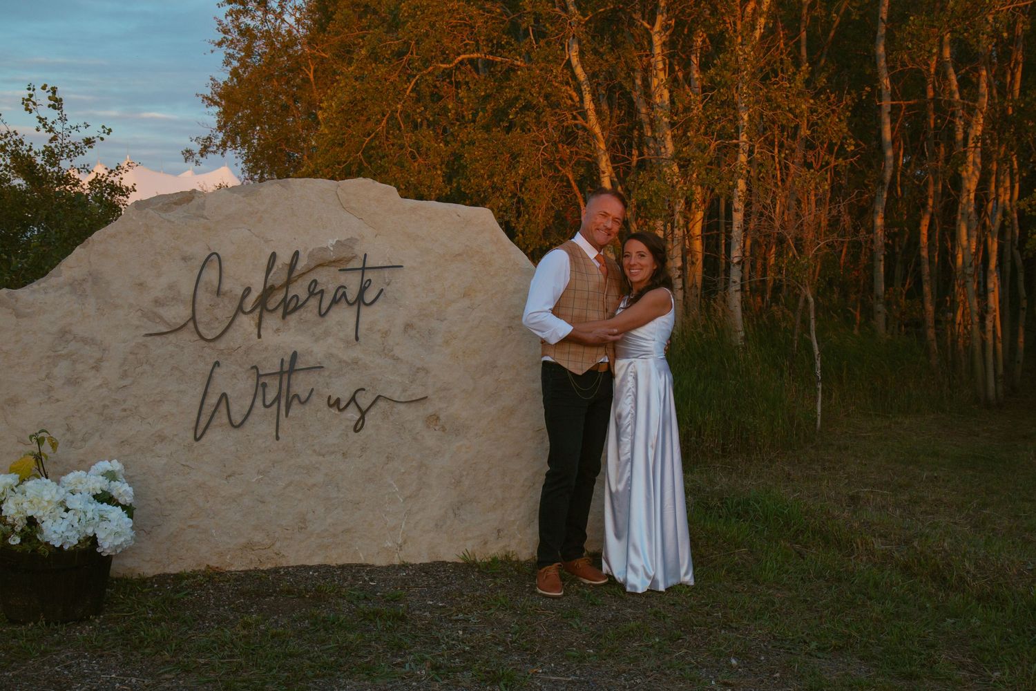 A couple dances together in a field at sunset with golden light filtering through trees.