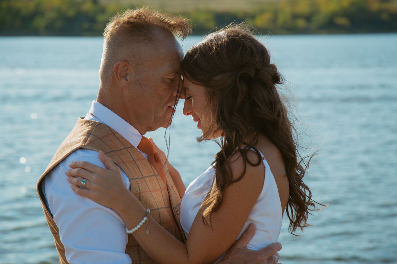Couple shares intimate forehead touch moment by waterfront.