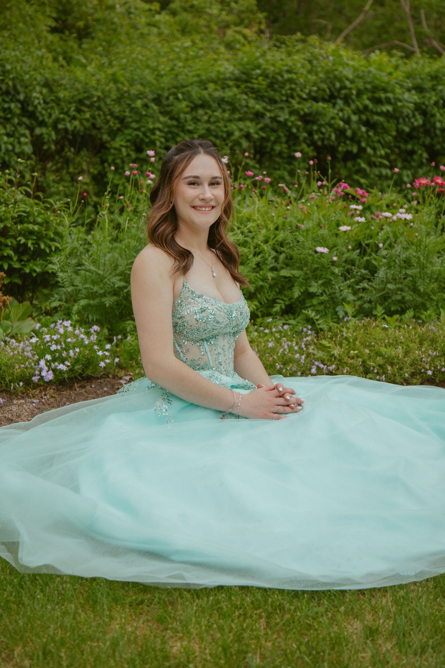 Young woman in mint green formal gown poses in blooming garden setting.