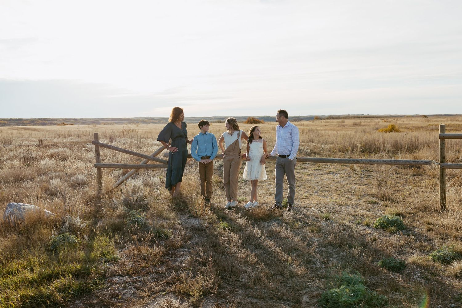 Family walking together on a grassy hillside during golden hour with scenic prairie landscape in the background.