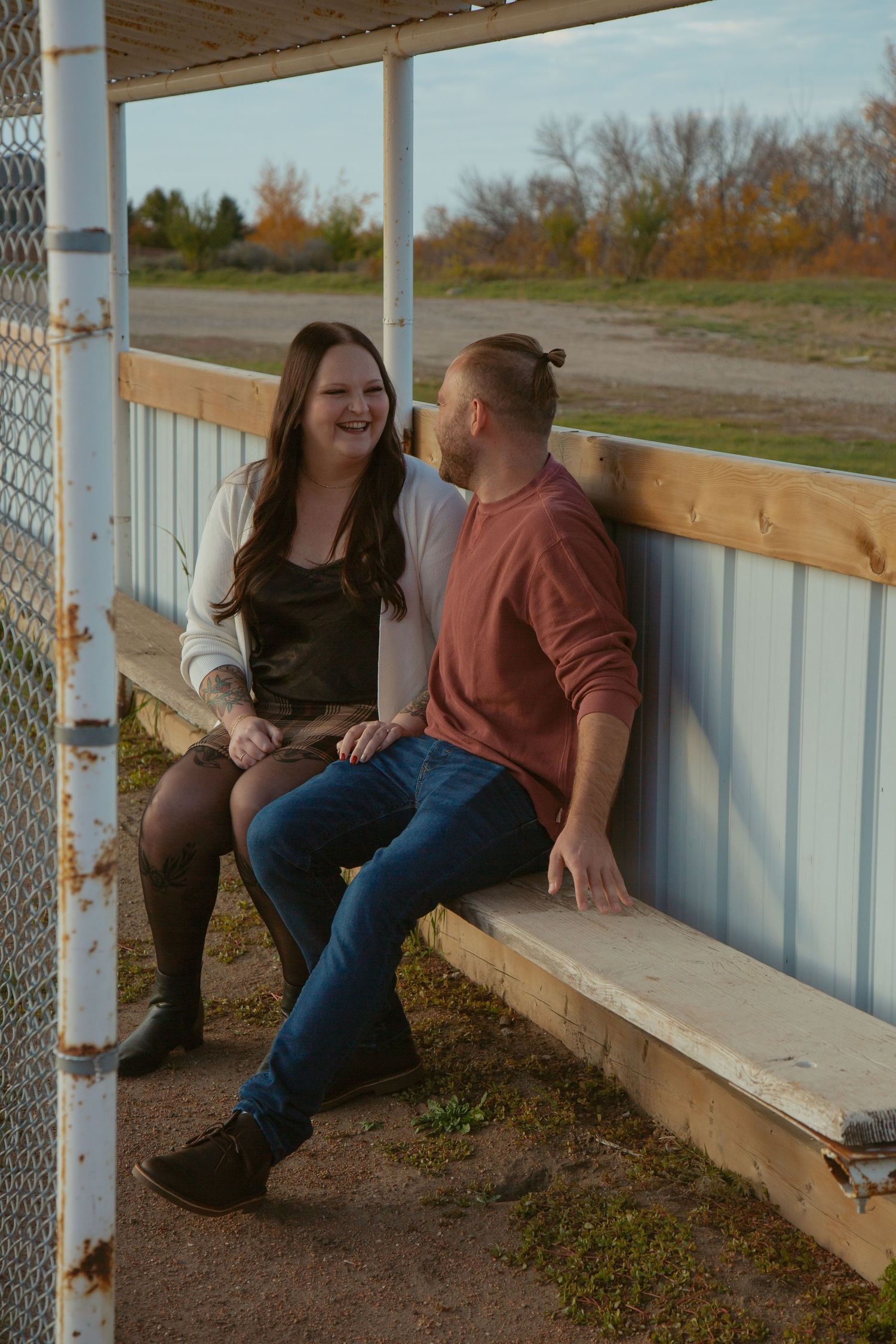 A couple shares a laugh while sitting on a wooden bench in a covered outdoor area.