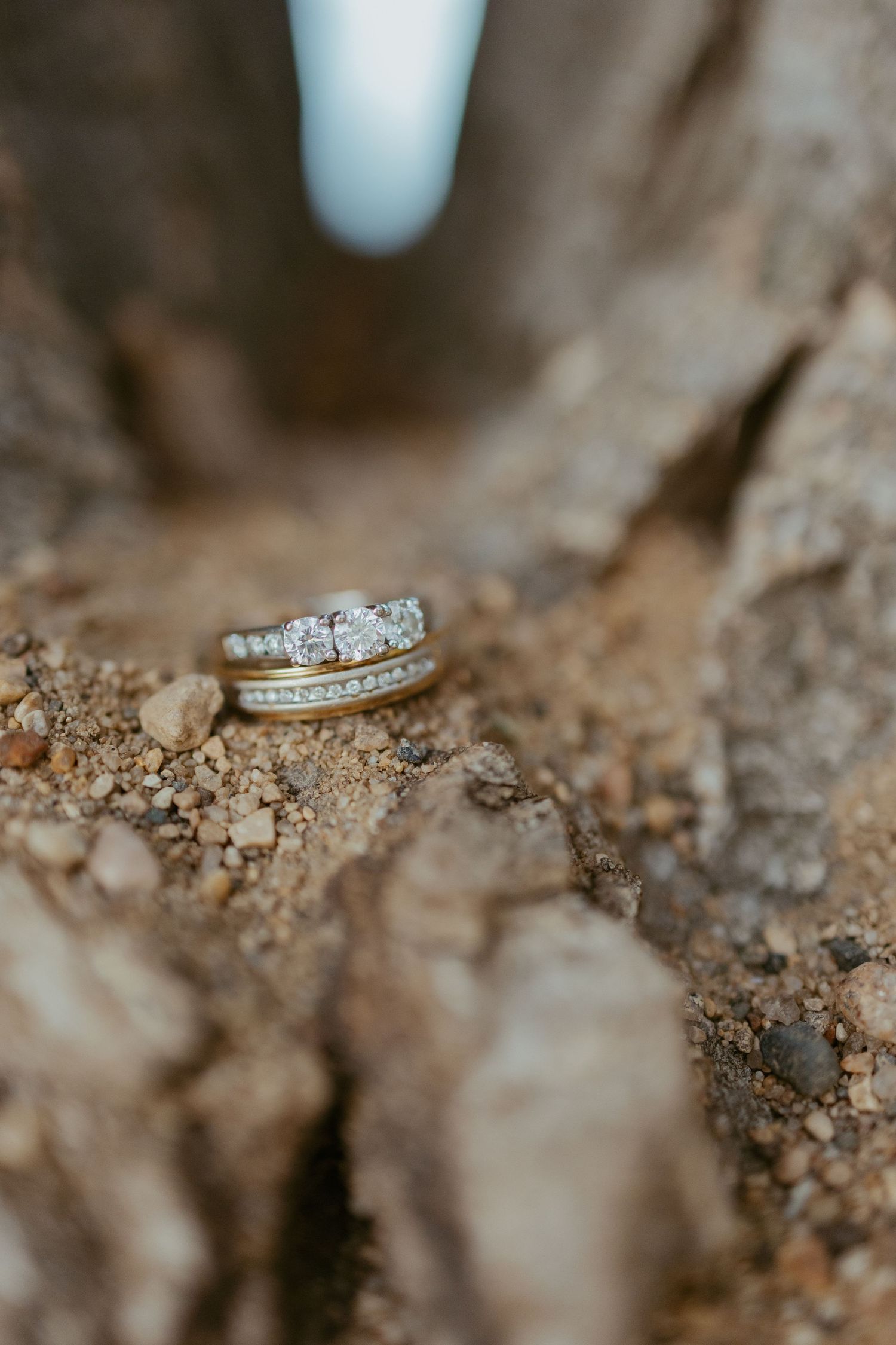 Diamond wedding rings nestled in brown soil with shallow depth of field.