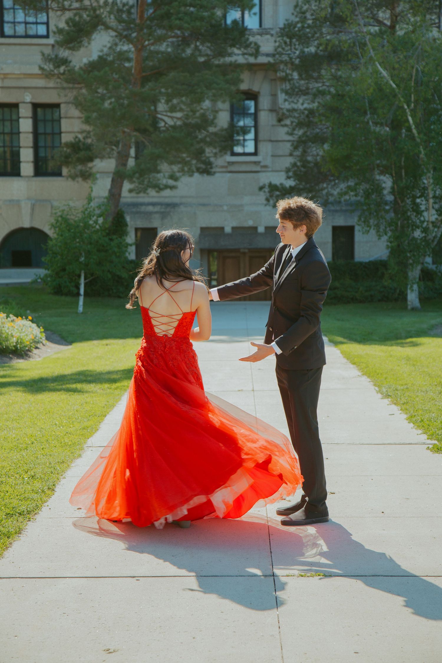 A flowing red formal dress twirls gracefully on a sunny pathway.