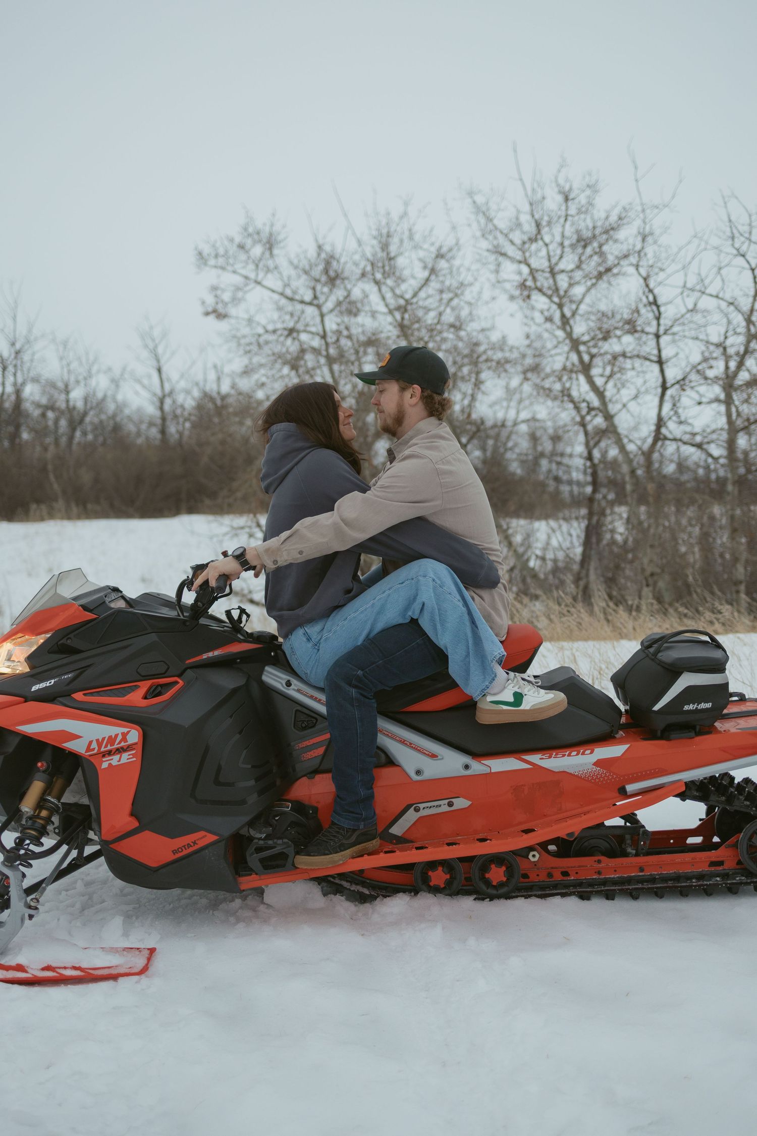 Couple sharing a romantic moment on a red Ski-Doo snowmobile in a snowy winter landscape.