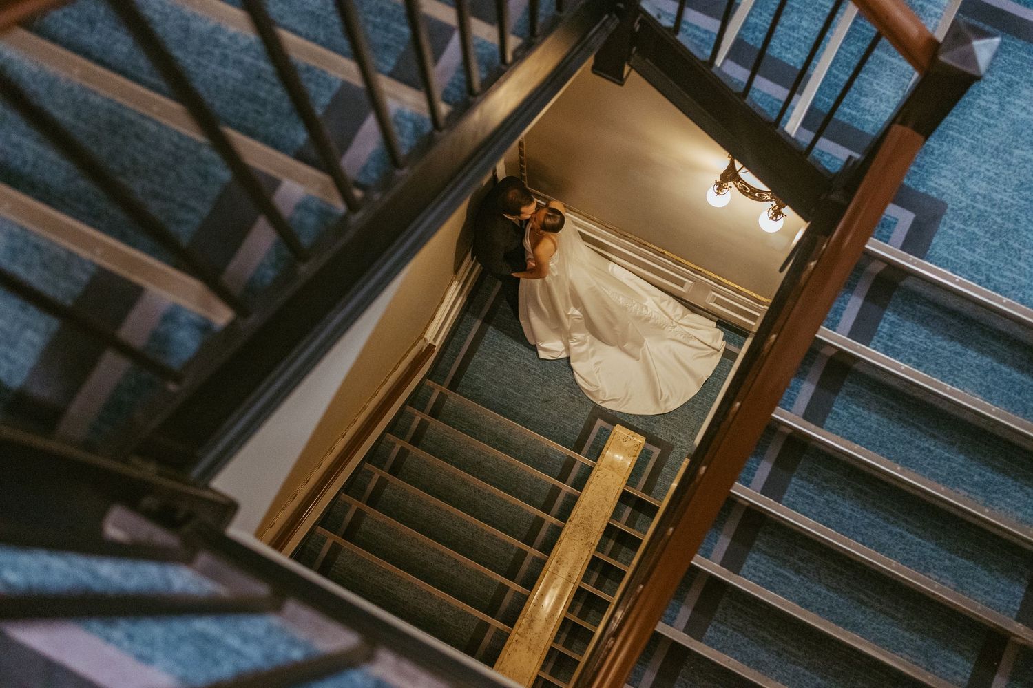 Aerial view of bride and groom sharing a romantic moment on carpeted staircase in elegant wedding venue.