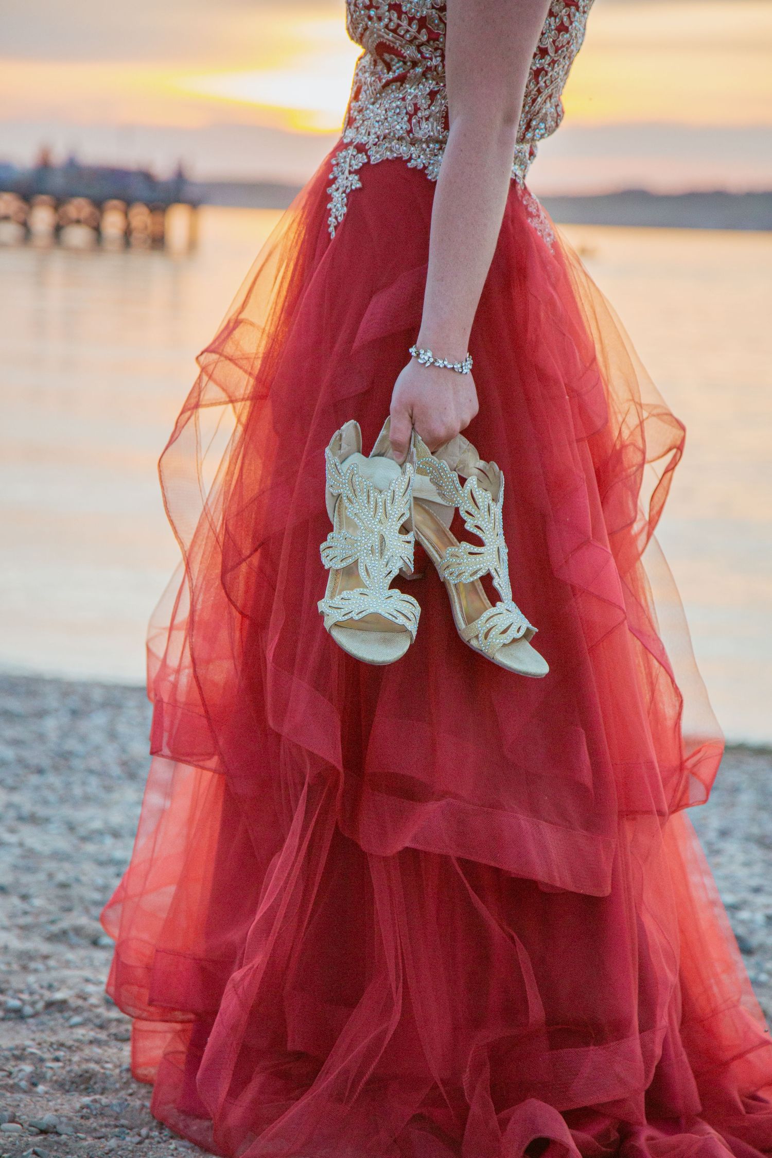 Red tulle formal dress photographed at sunset on beach with white shoes.