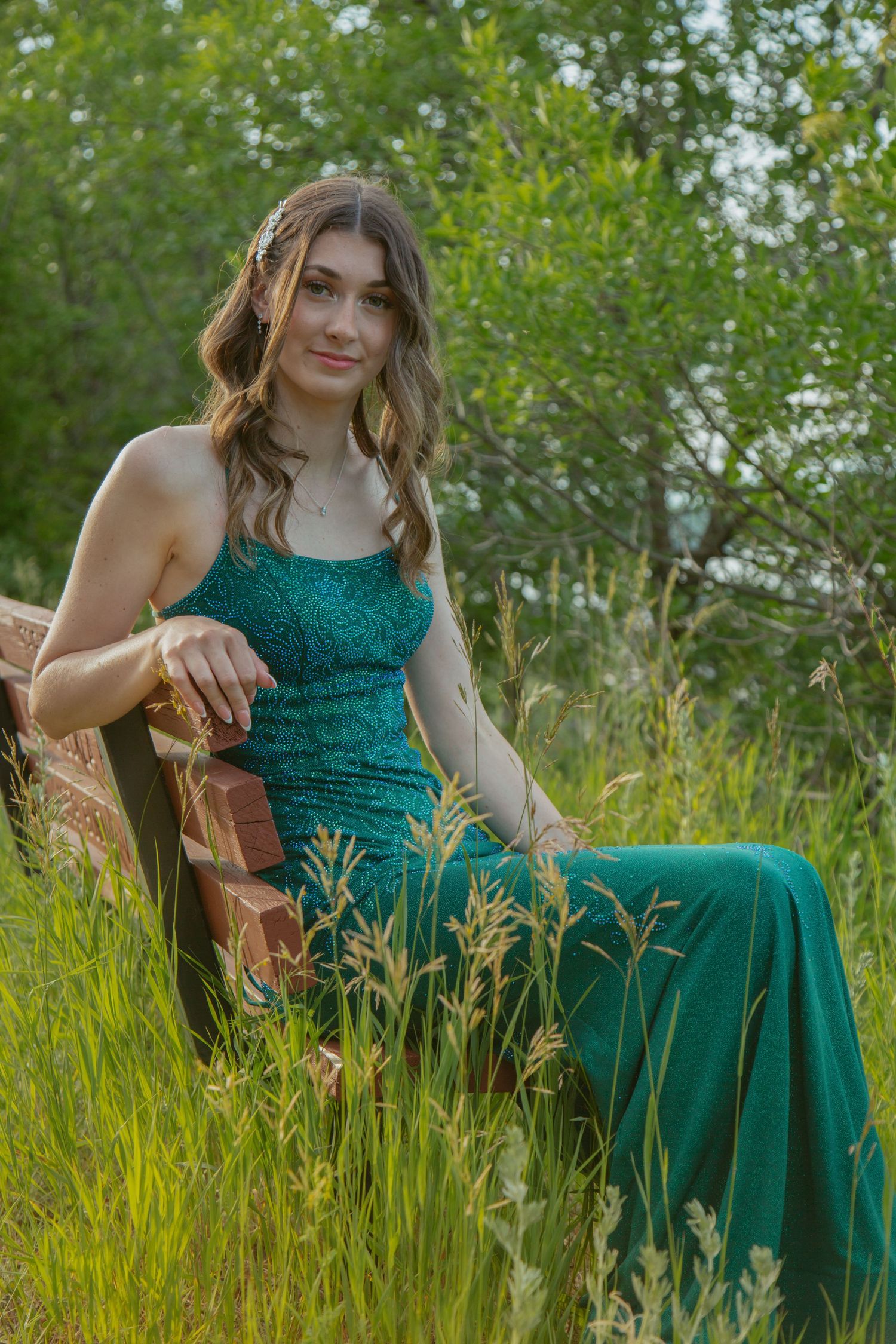 An emerald green formal dress sparkles in tall summer grass during an outdoor photo session.