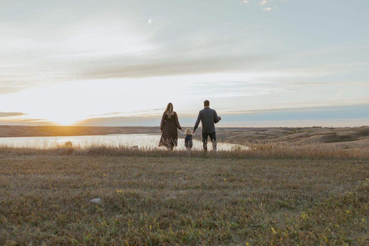 Silhouettes of people walking across a prairie landscape at dusk with dramatic sky.