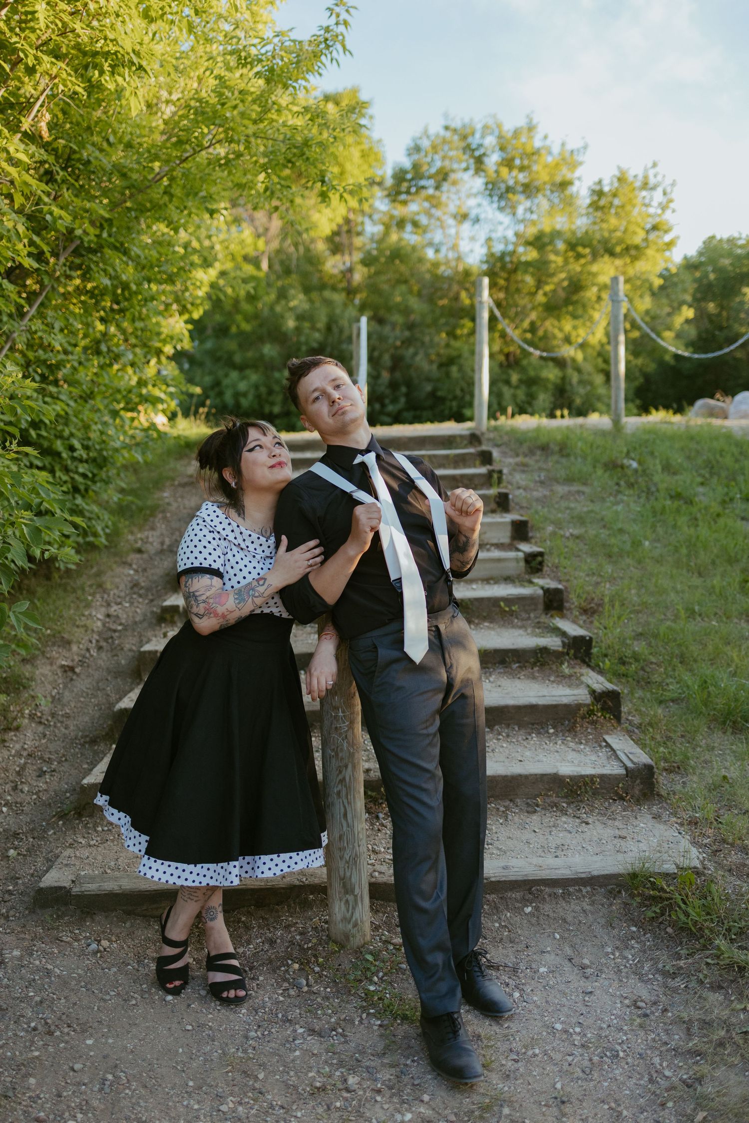Couple in retro clothing posing playfully on outdoor stone steps.