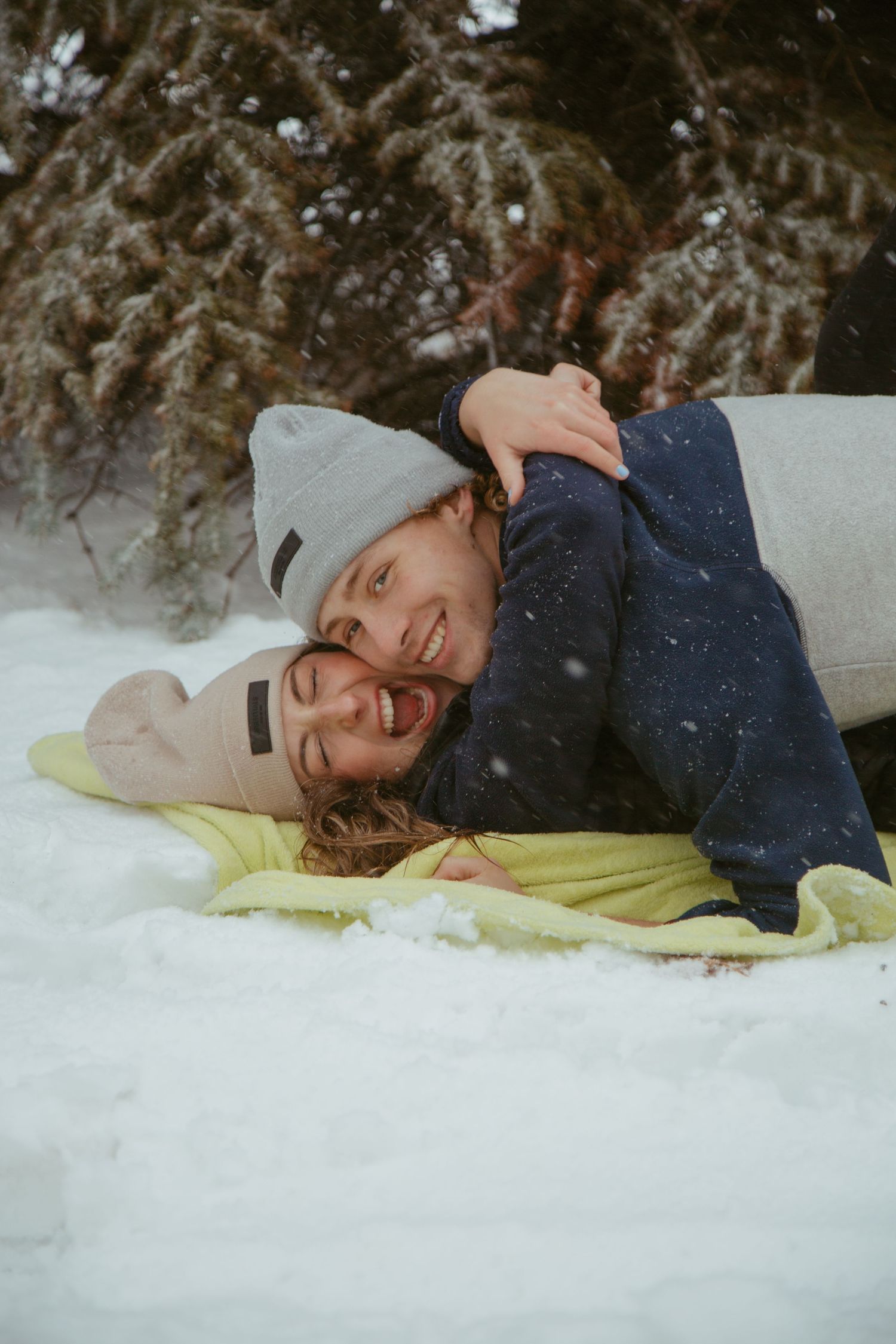Person lying playfully in the snow on a yellow blanket during a winter photoshoot.