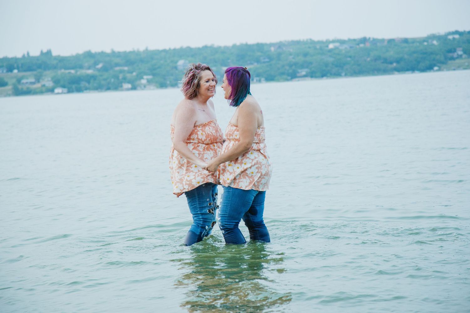 Couple embraces playfully in shallow turquoise water on a sunny day at the lake.