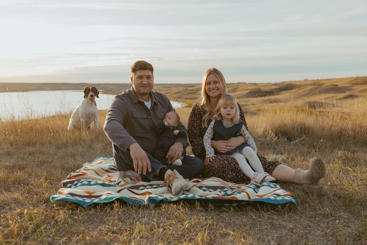 Family relaxing on a blanket in a scenic prairie field during golden hour.