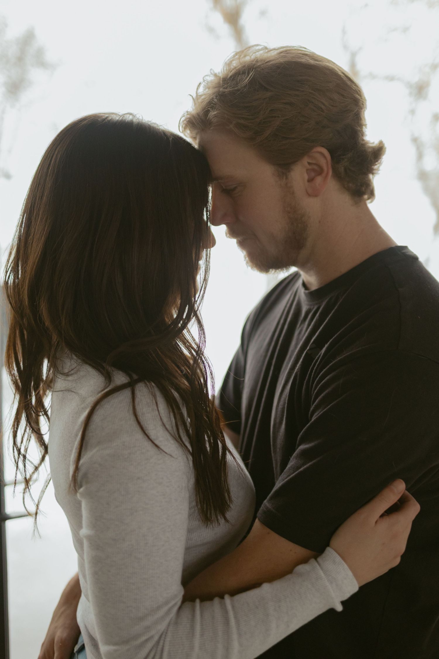A couple embraces intimately, touching foreheads in a tender romantic moment, man in black tee and woman in gray top.