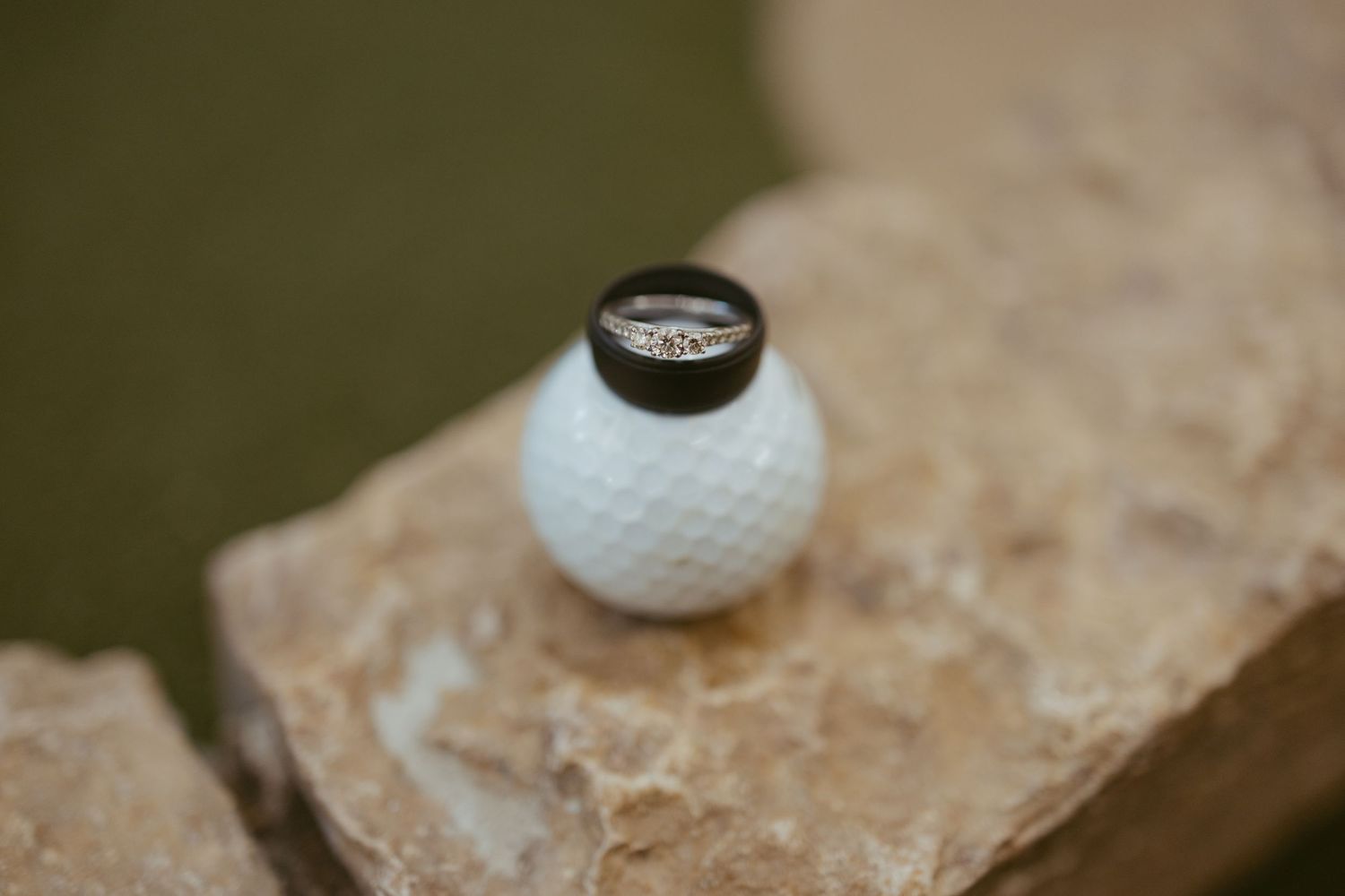 Wedding rings resting on a golf ball atop a stone surface for a golf-themed engagement.