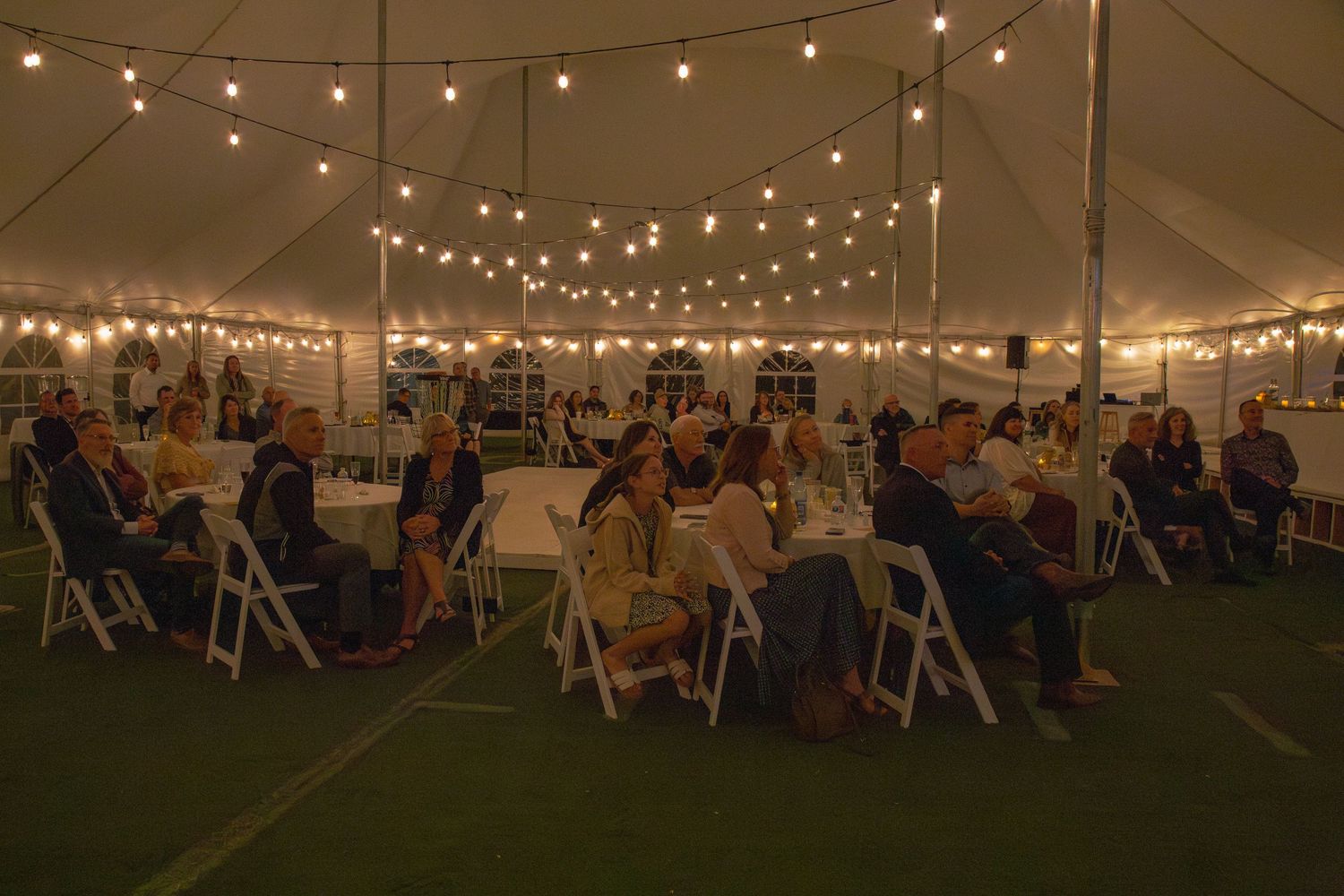 Wedding reception tent illuminated with string lights at dusk.