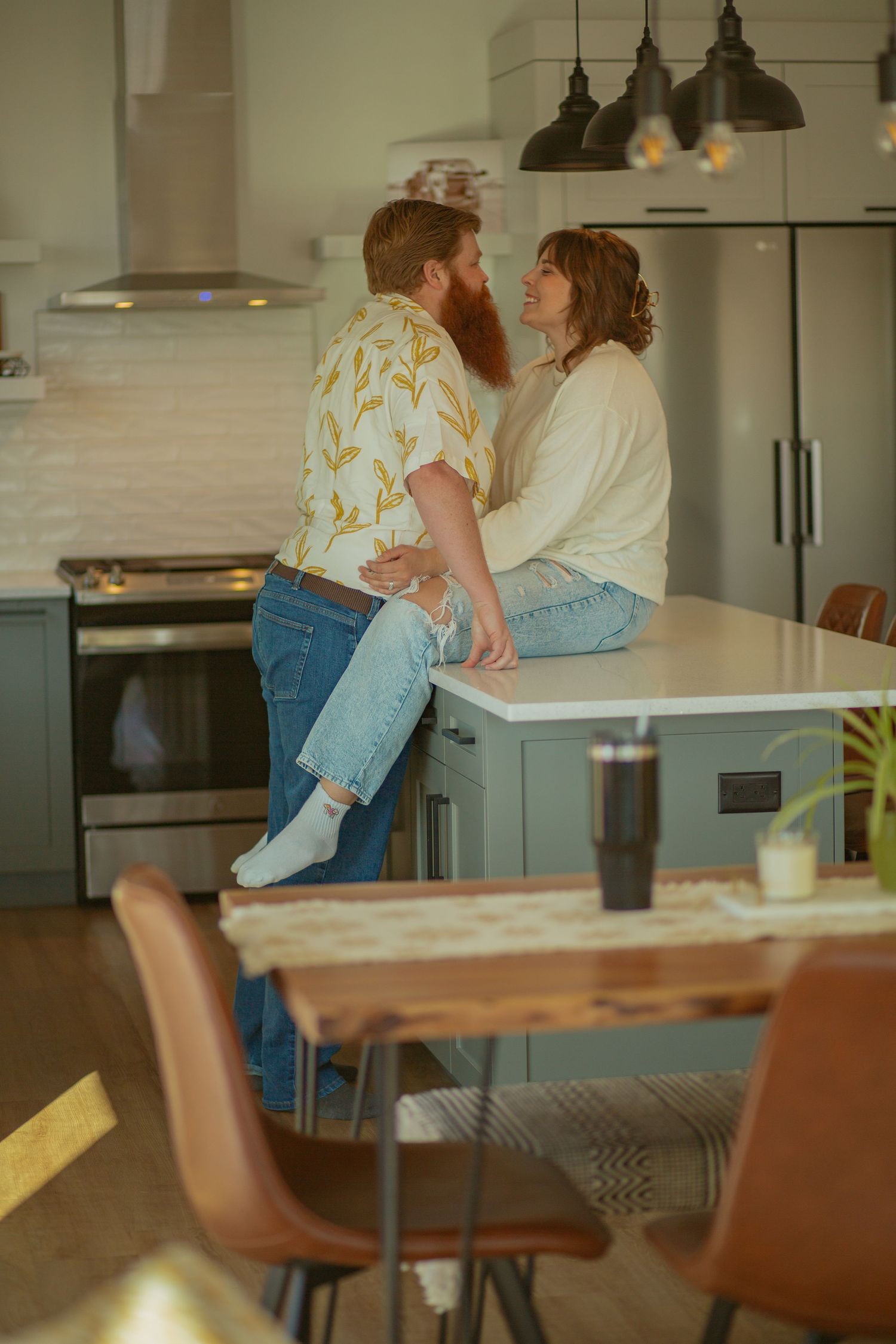 Romantic moment shared in a modern kitchen with pendant lights and wooden furniture.