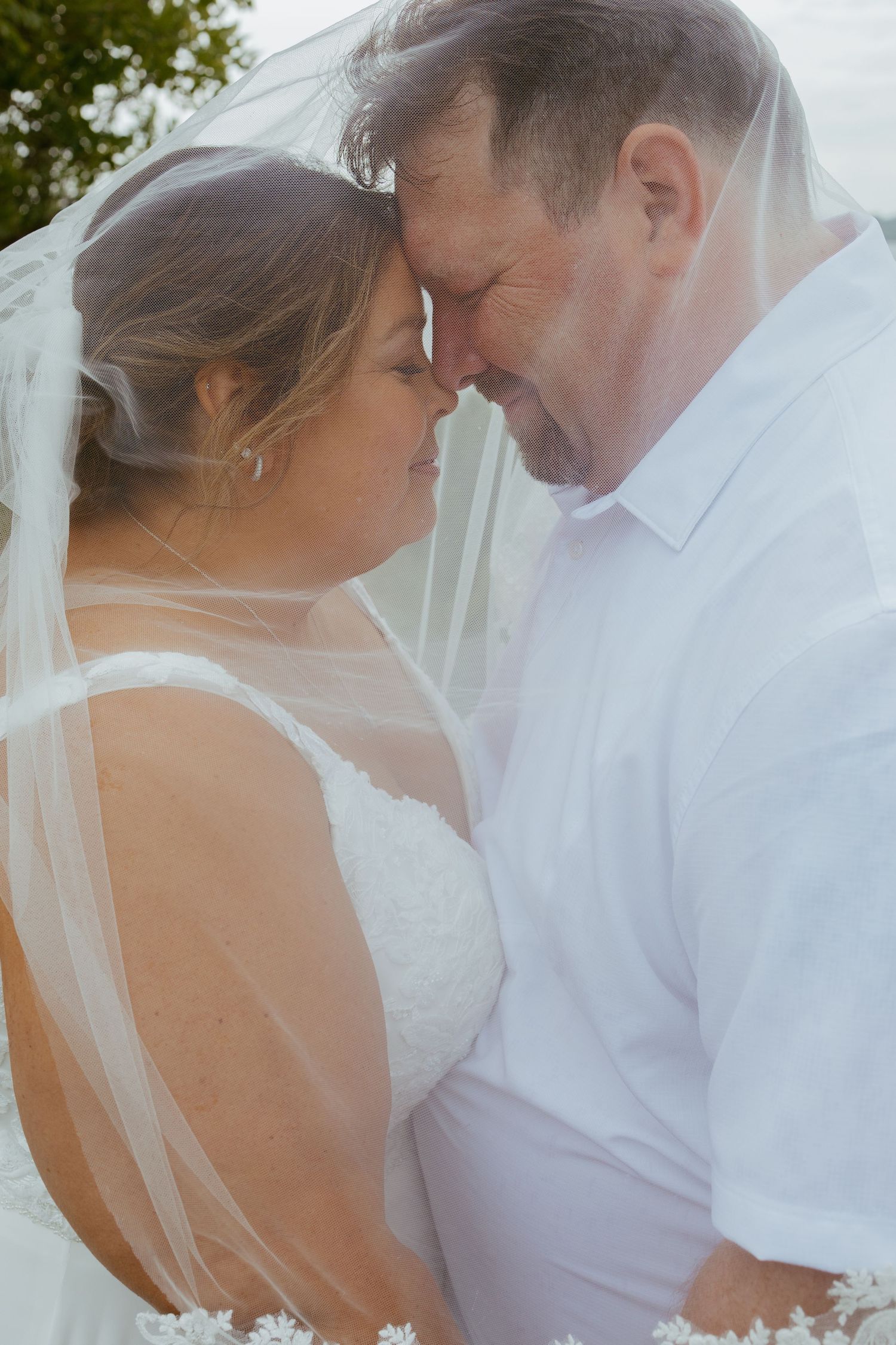 Bride and groom share an intimate forehead touch under a flowing white veil on their wedding day.